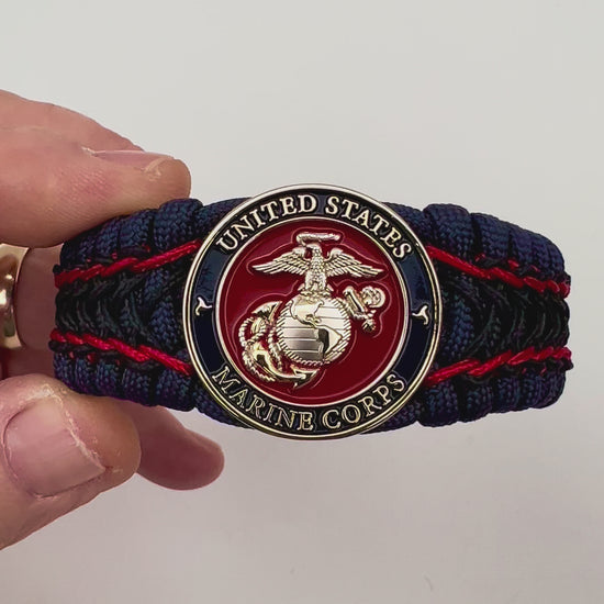 Thick and comfortable braided United States Marine Corps bracelet featuring a 24K gold and silver plated USMC officer Eagle Globe and Anchor medallion, a Cobra style tactical buckle and woven with gold 550 paracord and Imperial Red and Black micro cord.