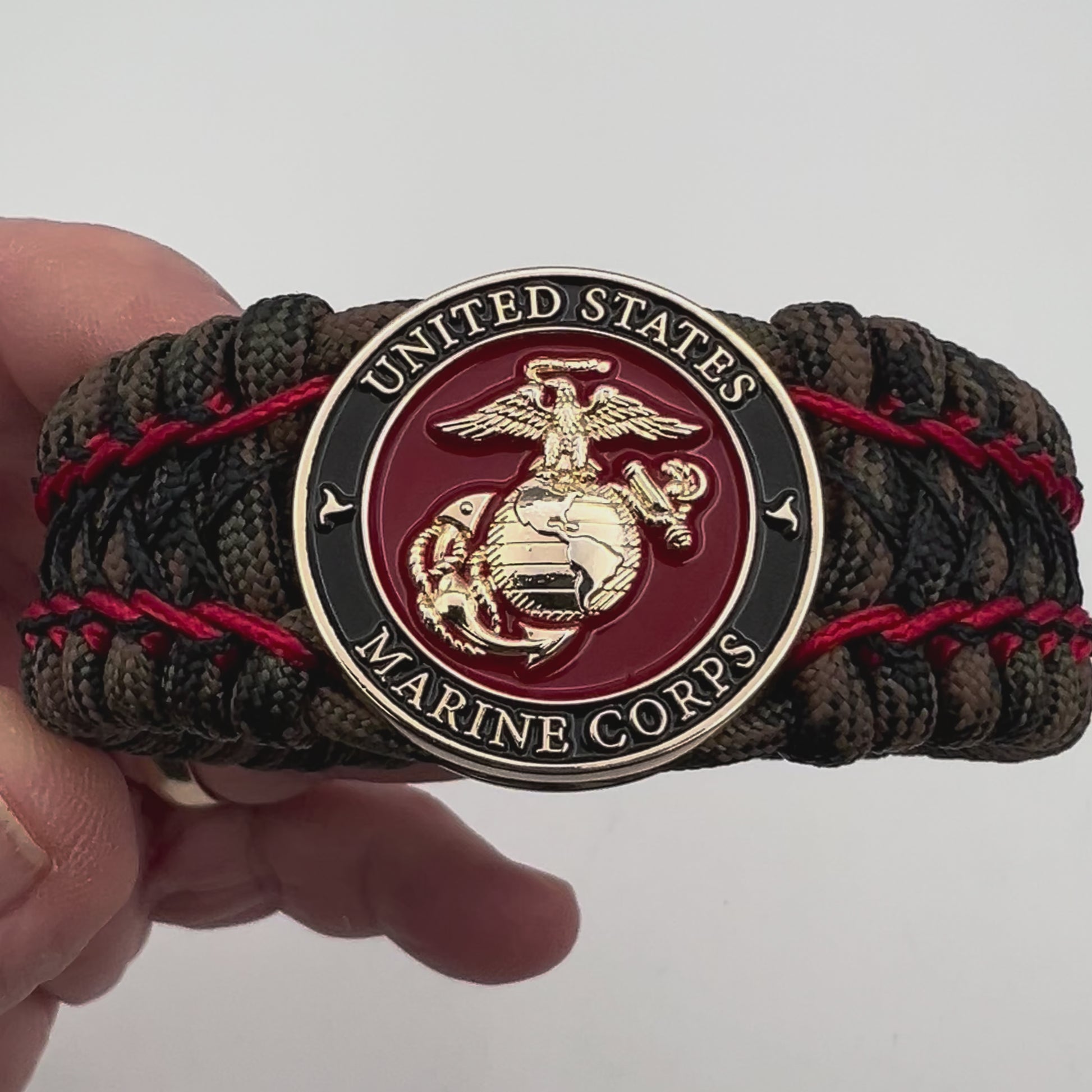 Thick, wide, rigid and comfortable braided United States Marine Corps bracelet featuring a 24K gold plated USMC Eagle Globe and Anchor medallion, a gold Cobra style tactical buckle and woven with Woodland Camo 550 paracord and Imperial Red micro and black nano cord.