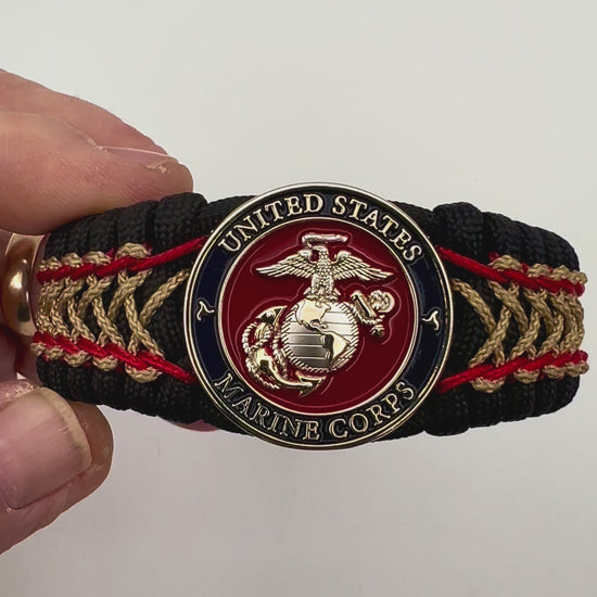 Thick and comfortable braided United States Marine Corps bracelet featuring a 24K gold and silver plated USMC officer Eagle Globe and Anchor medallion, a black Cobra style tactical buckle and woven with black 550 paracord and Imperial Red and gold micro cord.