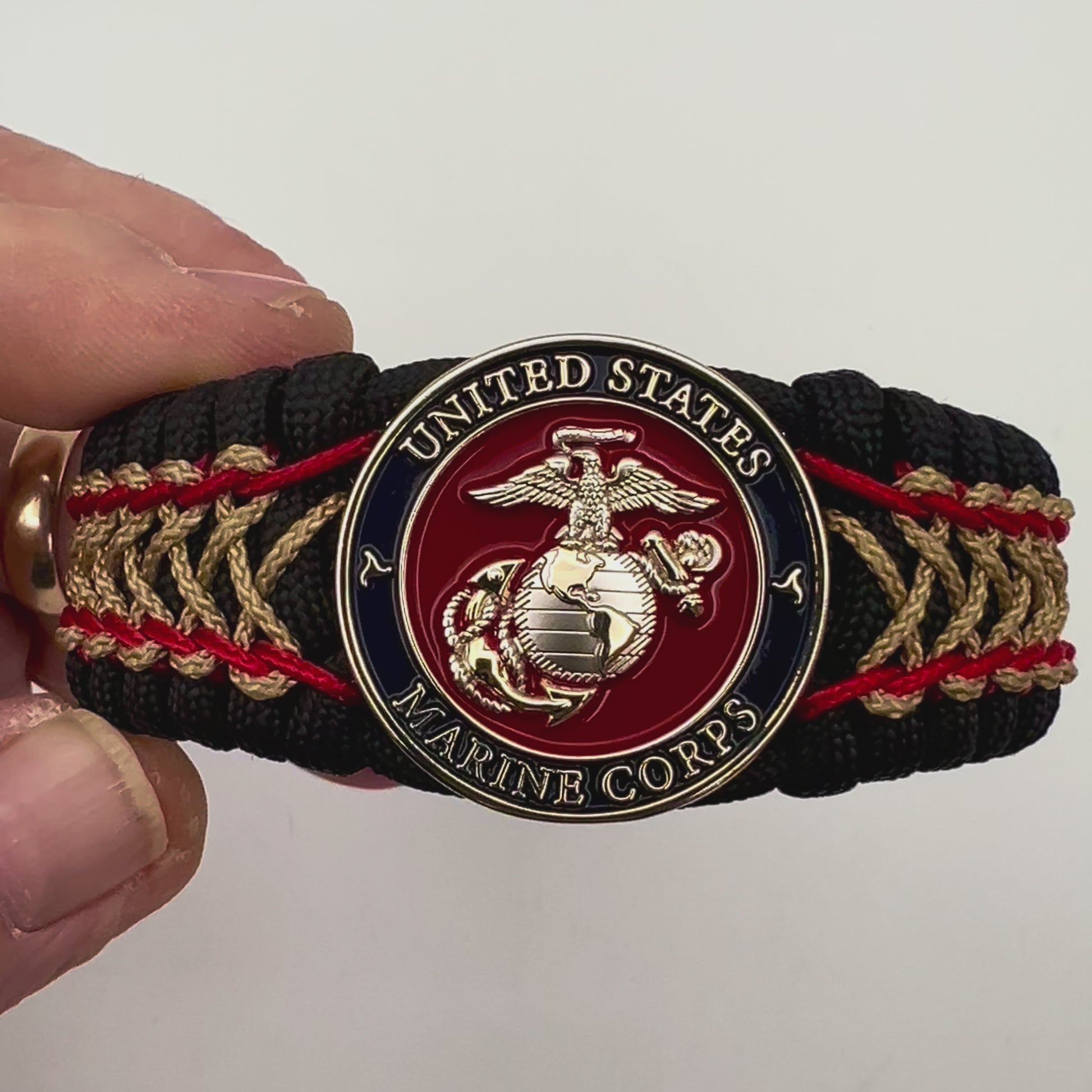 Thick and comfortable braided United States Marine Corps bracelet featuring a 24K gold and silver plated USMC officer Eagle Globe and Anchor medallion, a black Cobra style tactical buckle and woven with black 550 paracord and Imperial Red and gold micro cord.