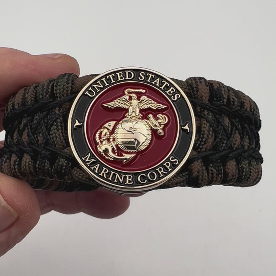 Thick, wide, rigid and comfortable braided United States Marine Corps bracelet featuring a 24K gold plated USMC Eagle Globe and Anchor medallion, a gold Cobra style tactical buckle and woven with Woodland Camo 550 paracord and black nano and micro cord.