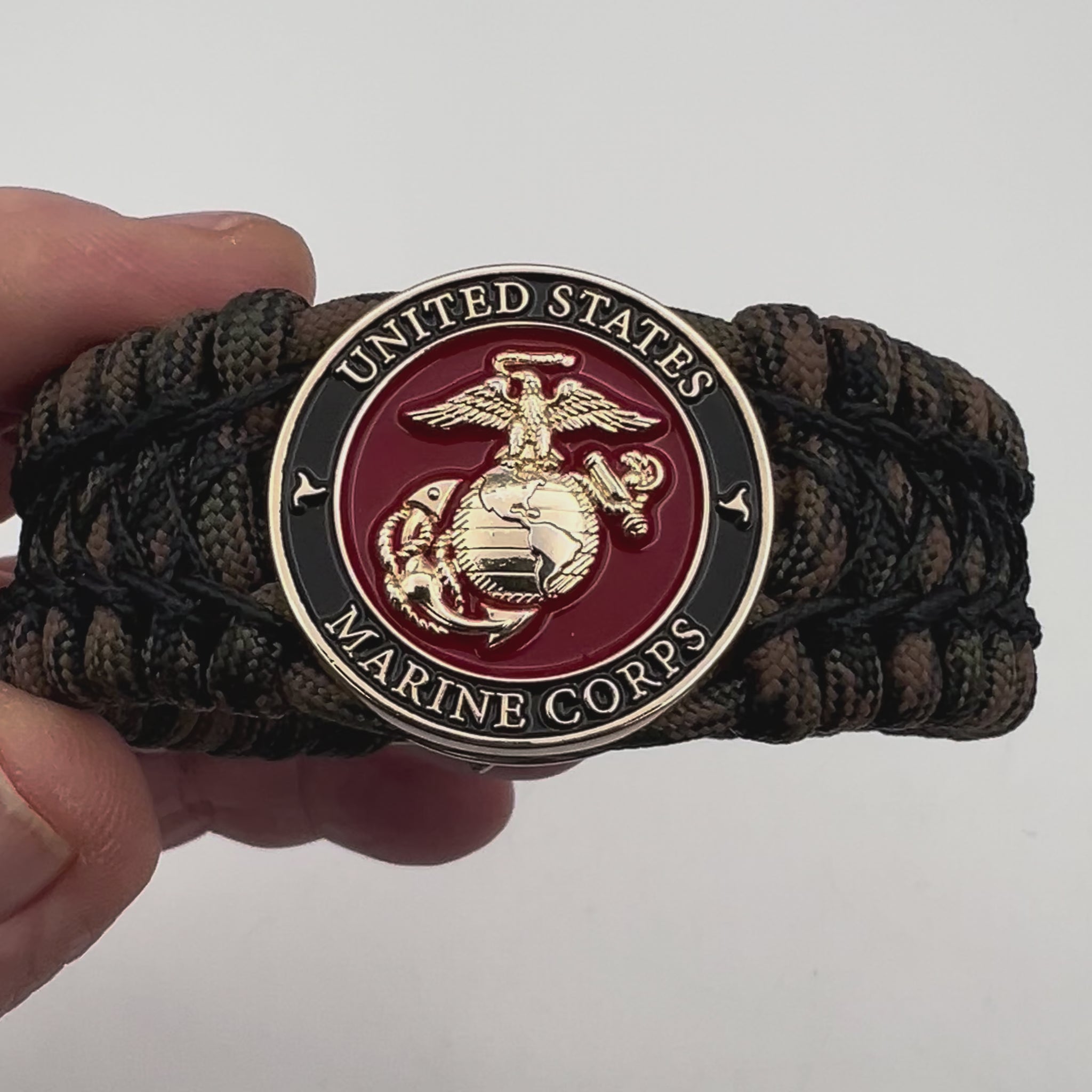 Thick, wide, rigid and comfortable braided United States Marine Corps bracelet featuring a 24K gold plated USMC Eagle Globe and Anchor medallion, a gold Cobra style tactical buckle and woven with Woodland Camo 550 paracord and black nano and micro cord.