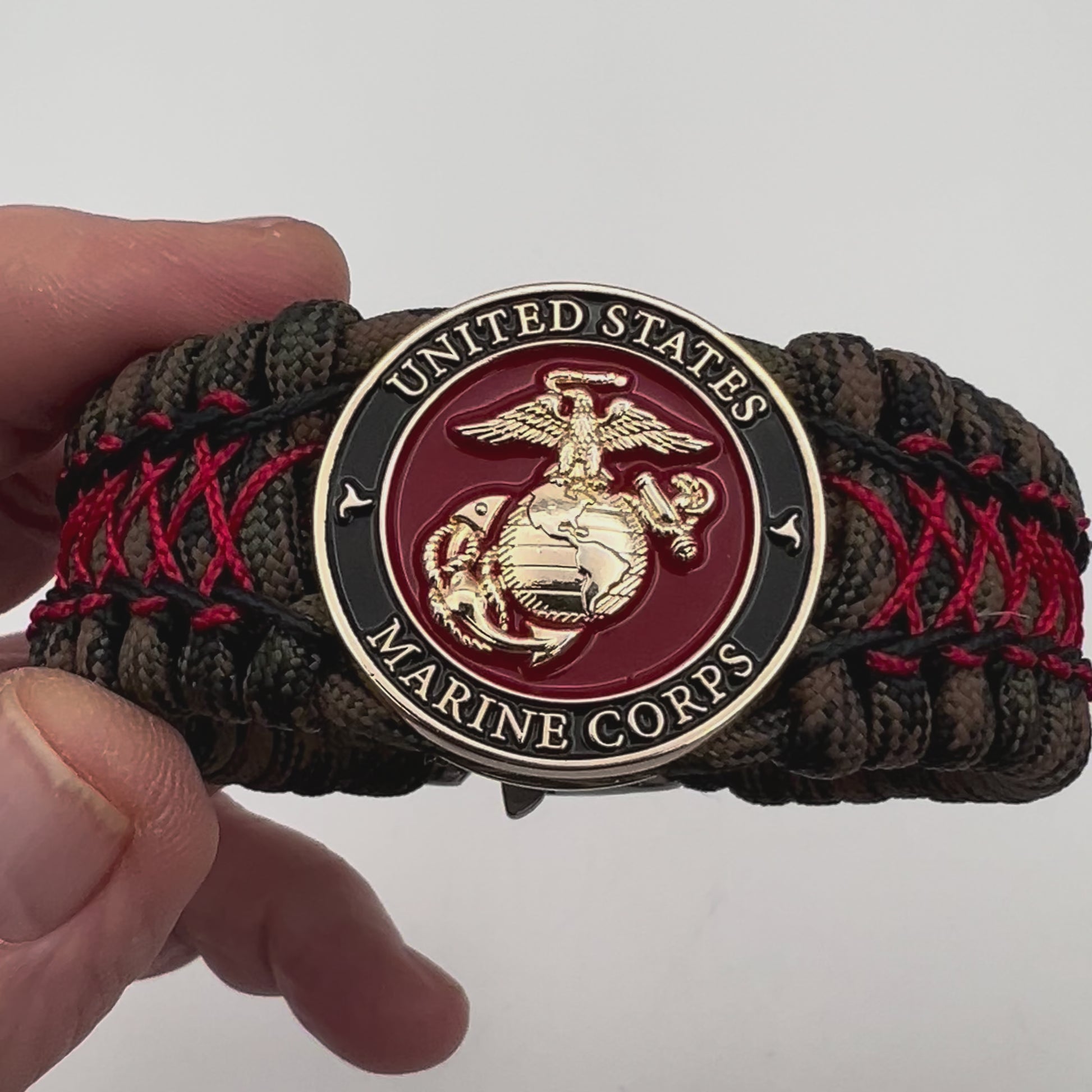 Thick, wide, rigid and comfortable braided United States Marine Corps bracelet featuring a 24K gold plated USMC Eagle Globe and Anchor medallion, a gold Cobra style tactical buckle and woven with Woodland Camo 550 paracord and Imperial Red micro and black nano cord.