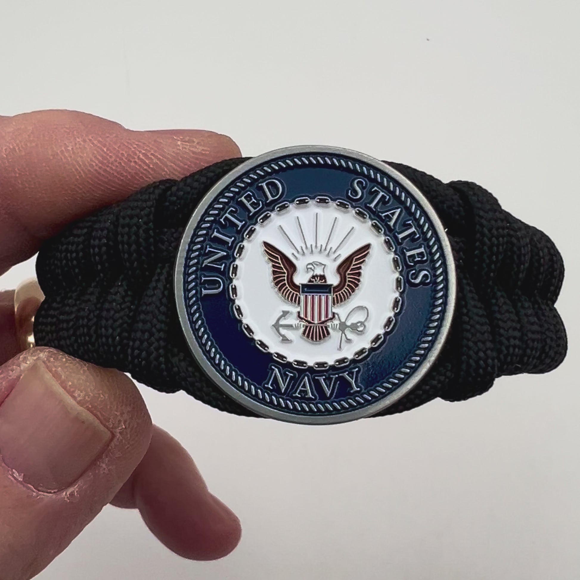 Thick, narrow, and semi-rigid braided United States Navy bracelet featuring an antique silver plated Navy medallion, a black Cobra style tactical buckle and woven with black 550 paracord.