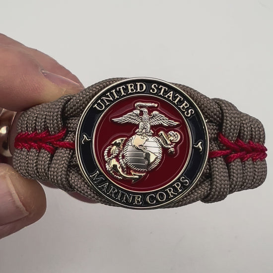 Thick, semi-rigid and comfortable braided United States Marine Corps bracelet featuring a 24K gold and silver plated USMC officer Eagle Globe and Anchor medallion, a gold Cobra style tactical buckle and woven with tan 550 paracord and Imperial red micro cord.