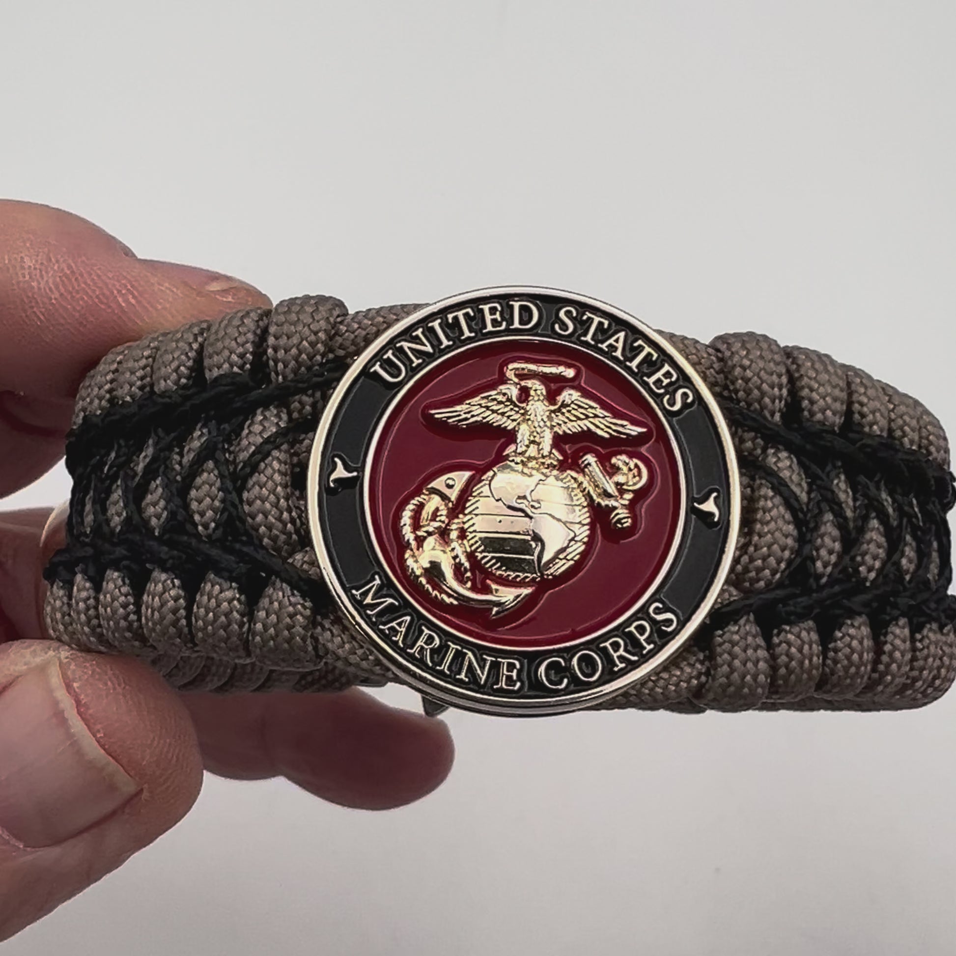 Thick, wide, rigid and comfortable braided United States Marine Corps bracelet featuring a 24K gold plated USMC Eagle Globe and Anchor medallion, a gold Cobra style tactical buckle and woven with tan 550 paracord and black nano and micro cord.