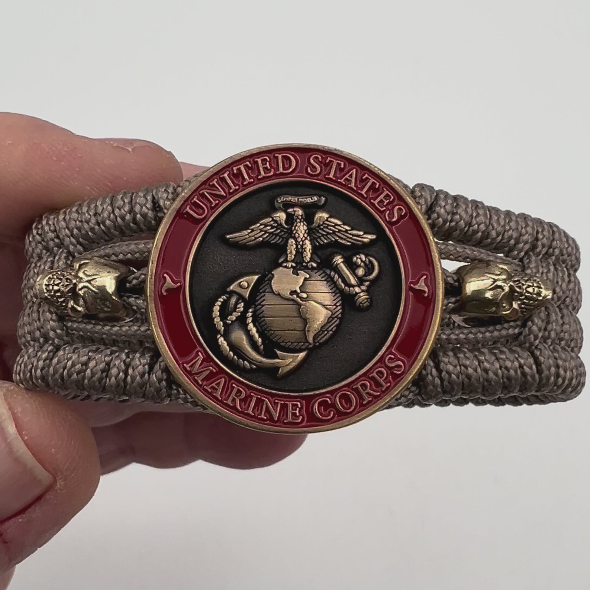 Thin, medium width, flexible and comfortable braided United States Marine Corps bracelet featuring a 24K antique gold plated USMC officer Eagle Globe and Anchor medallion, two gold plated skulls, a gold Cobra style tactical buckle and woven with tan Type-1 paracord.