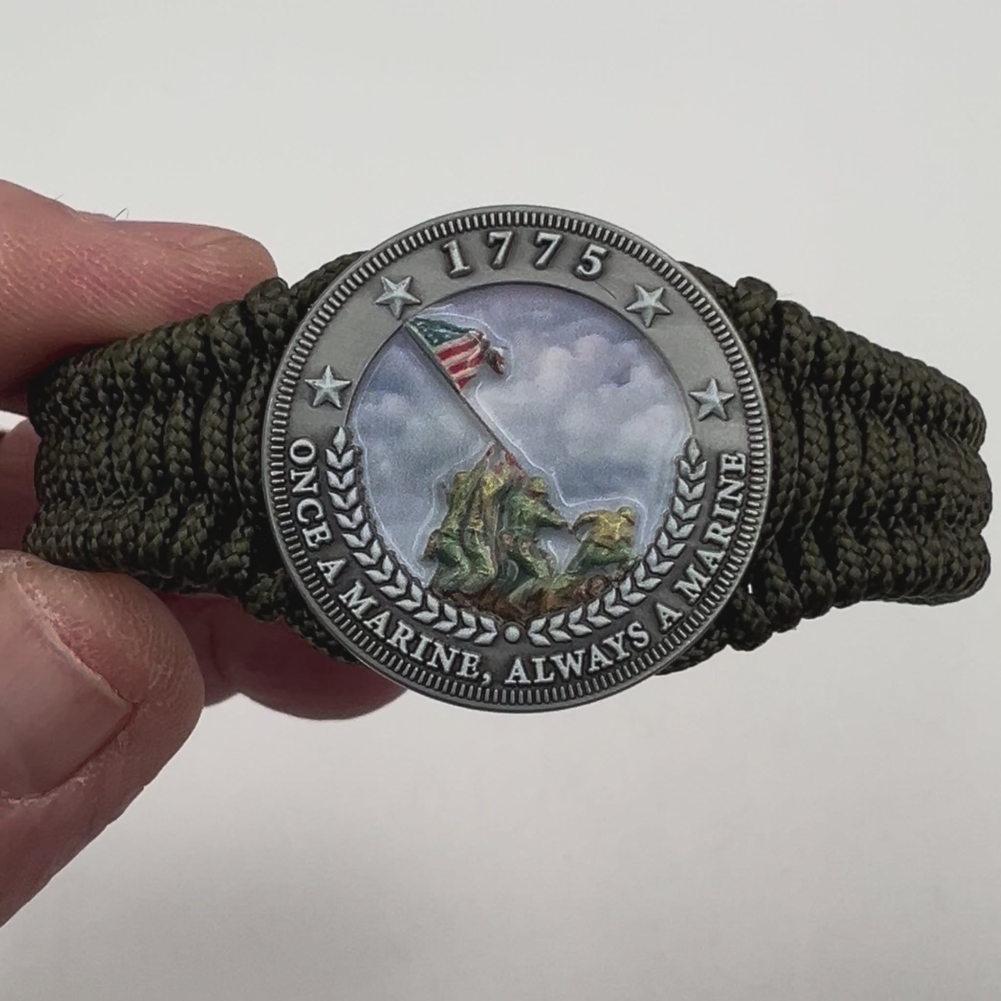 Thin, narrow, flexible and comfortable braided United States Marine Corps Iwo Jima bracelet featuring an antique silver plated UV painted Iwo Jima flag raising medallion, a silver Cobra style tactical buckle and woven with Olive Drab type-1 paracord.
