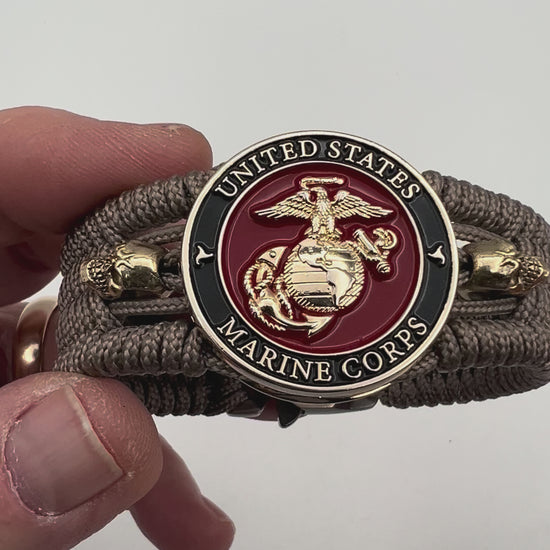 Thin, medium width, flexible and comfortable braided United States Marine Corps bracelet featuring a 24K gold plated USMC officer Eagle Globe and Anchor medallion, two gold plated skulls, a gold Cobra style tactical buckle and woven with Tan Type-1 paracord.