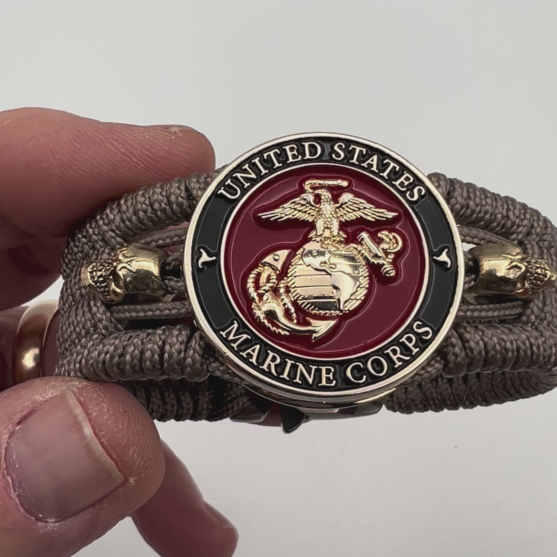 Thin, medium width, flexible and comfortable braided United States Marine Corps bracelet featuring a 24K gold plated USMC officer Eagle Globe and Anchor medallion, two gold plated skulls, a gold Cobra style tactical buckle and woven with Tan Type-1 paracord.