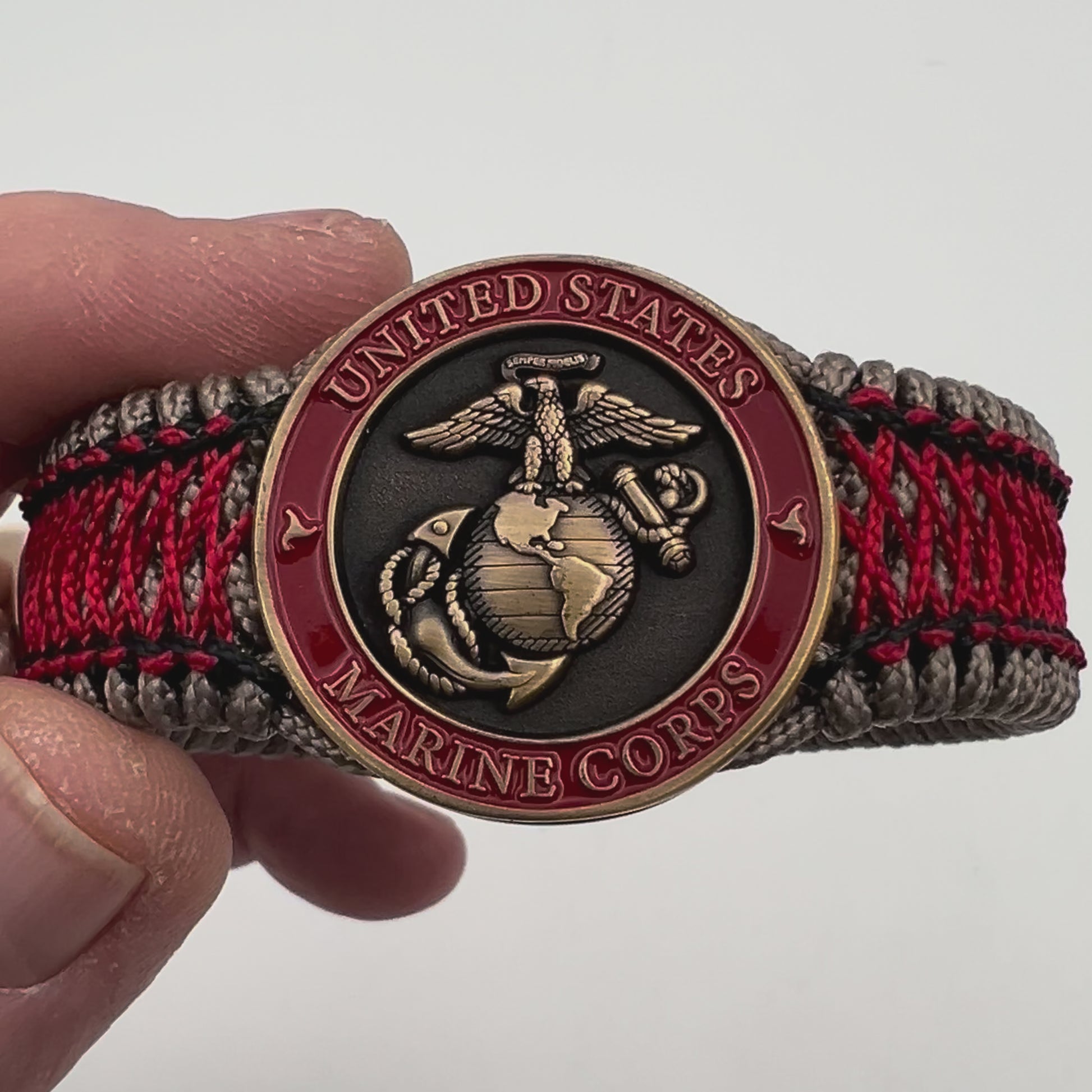 Thin, medium width, flexible and comfortable braided United States Marine Corps bracelet featuring a 24K antique gold plated USMC Eagle Globe and Anchor medallion, a gold Cobra style tactical buckle and woven with Tan Type-1 paracord and Imperial Red and Black nano cord.