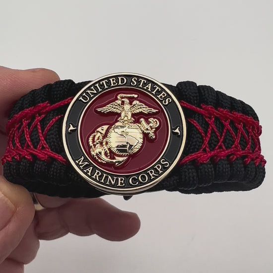 Thick, wide, rigid and comfortable braided United States Marine Corps bracelet featuring a 24K gold plated USMC Eagle Globe and Anchor medallion, a black Cobra style tactical buckle and woven with black 550 paracord and Imperial Red nano and micro cord.