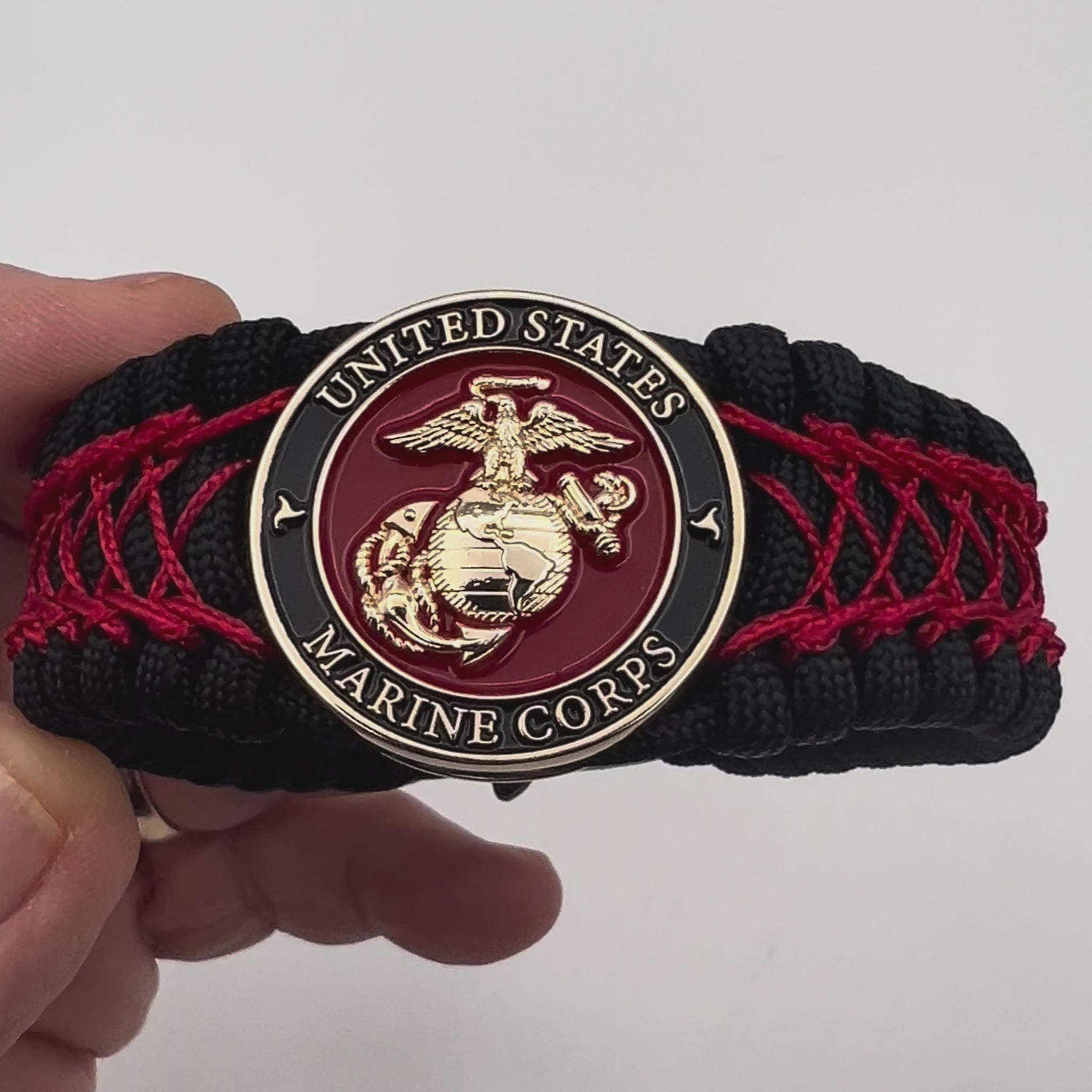 Thick, wide, rigid and comfortable braided United States Marine Corps bracelet featuring a 24K gold plated USMC Eagle Globe and Anchor medallion, a black Cobra style tactical buckle and woven with black 550 paracord and Imperial Red nano and micro cord.