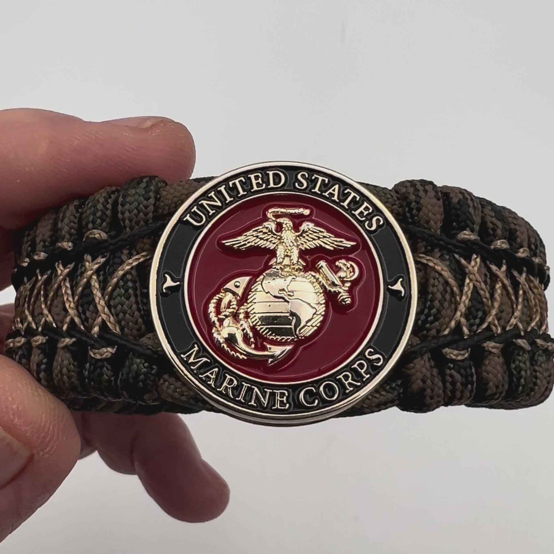 Thick, wide, rigid and comfortable braided United States Marine Corps bracelet featuring a 24K gold plated USMC Eagle Globe and Anchor medallion, a gold Cobra style tactical buckle and woven with Woodland 550 paracord, black micro and tan nano cord.
