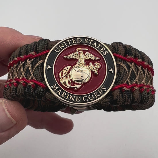 Thick, wide, rigid and comfortable braided United States Marine Corps bracelet featuring a 24K gold plated USMC Eagle Globe and Anchor medallion, a gold Cobra style tactical buckle and woven with Woodland Camo 550 paracord and Imperial Red micro and gold nano cord.