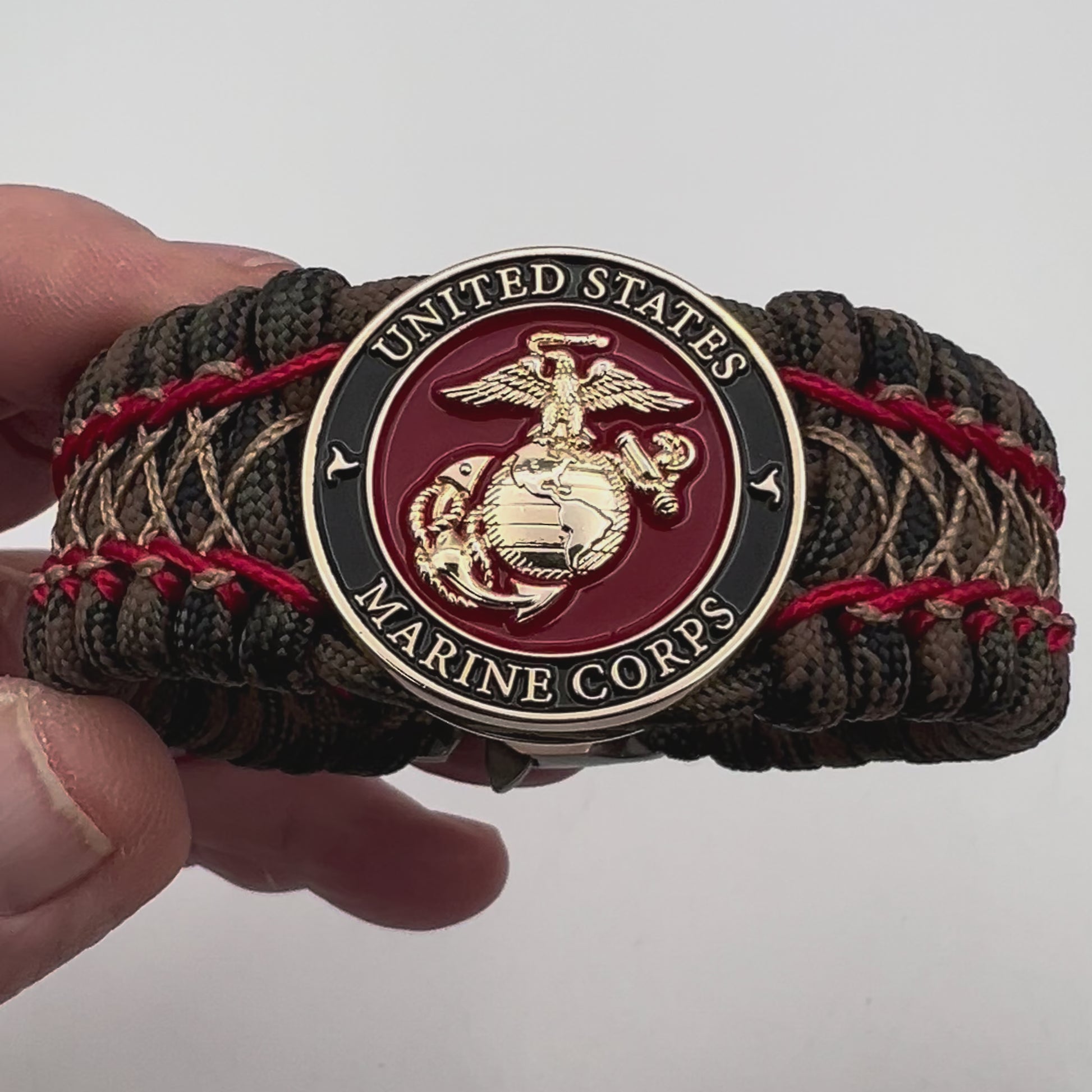 Thick, wide, rigid and comfortable braided United States Marine Corps bracelet featuring a 24K gold plated USMC Eagle Globe and Anchor medallion, a gold Cobra style tactical buckle and woven with Woodland Camo 550 paracord and Imperial Red micro and gold nano cord.