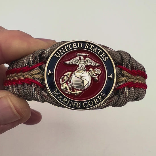Thick and comfortable braided United States Marine Corps bracelet featuring a 24K gold and silver plated USMC officer Eagle Globe and Anchor medallion, a Cobra style tactical buckle and woven with Desert Camo 550 paracord and Imperial red and gold micro cord.