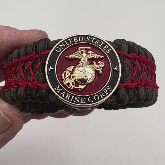 Thick, wide, rigid and comfortable braided United States Marine Corps bracelet featuring a 24K gold plated USMC Eagle Globe and Anchor medallion, a gold Cobra style tactical buckle and woven with Woodland Camo 550 paracord and Imperial Red nano and micro cord.