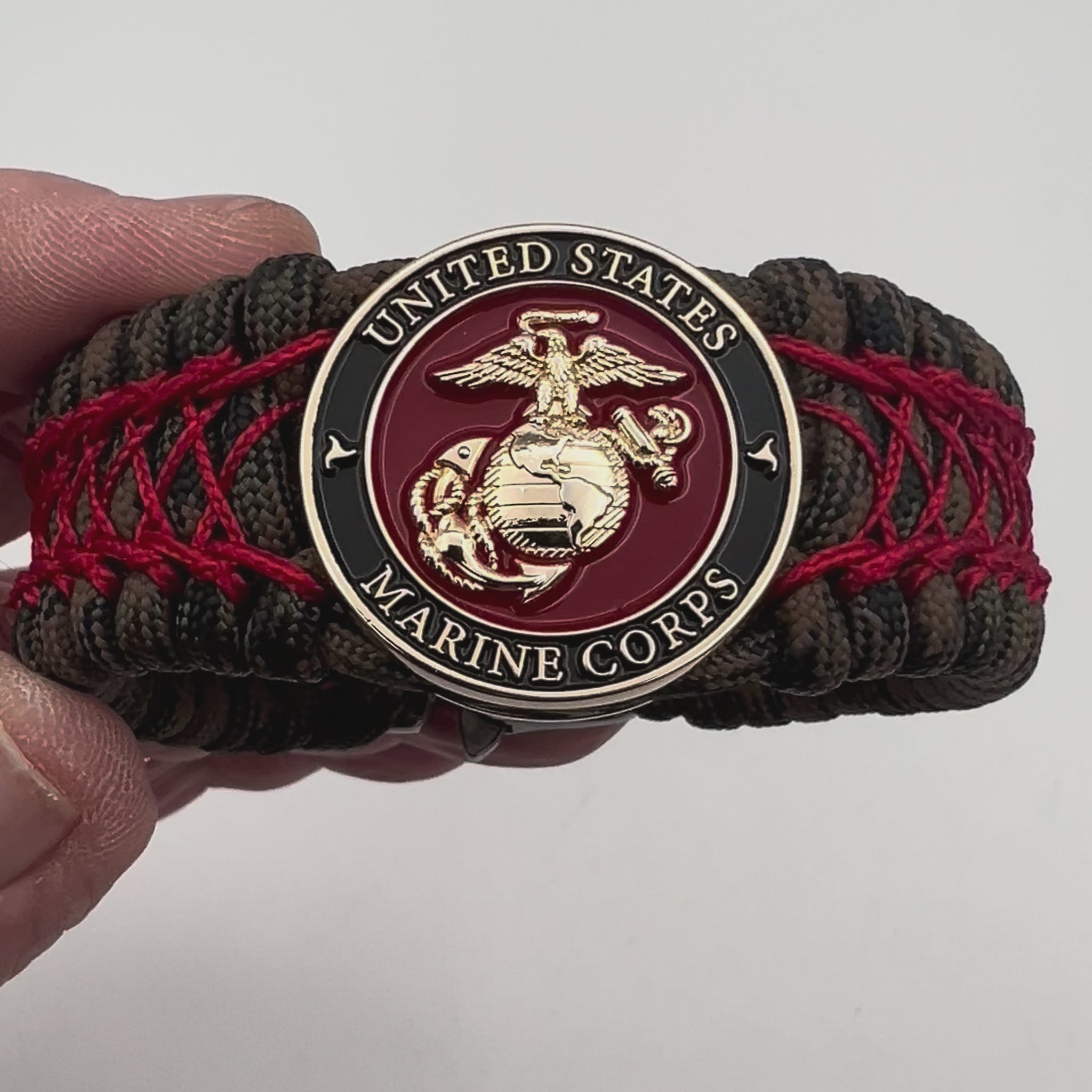 Thick, wide, rigid and comfortable braided United States Marine Corps bracelet featuring a 24K gold plated USMC Eagle Globe and Anchor medallion, a gold Cobra style tactical buckle and woven with Woodland Camo 550 paracord and Imperial Red nano and micro cord.