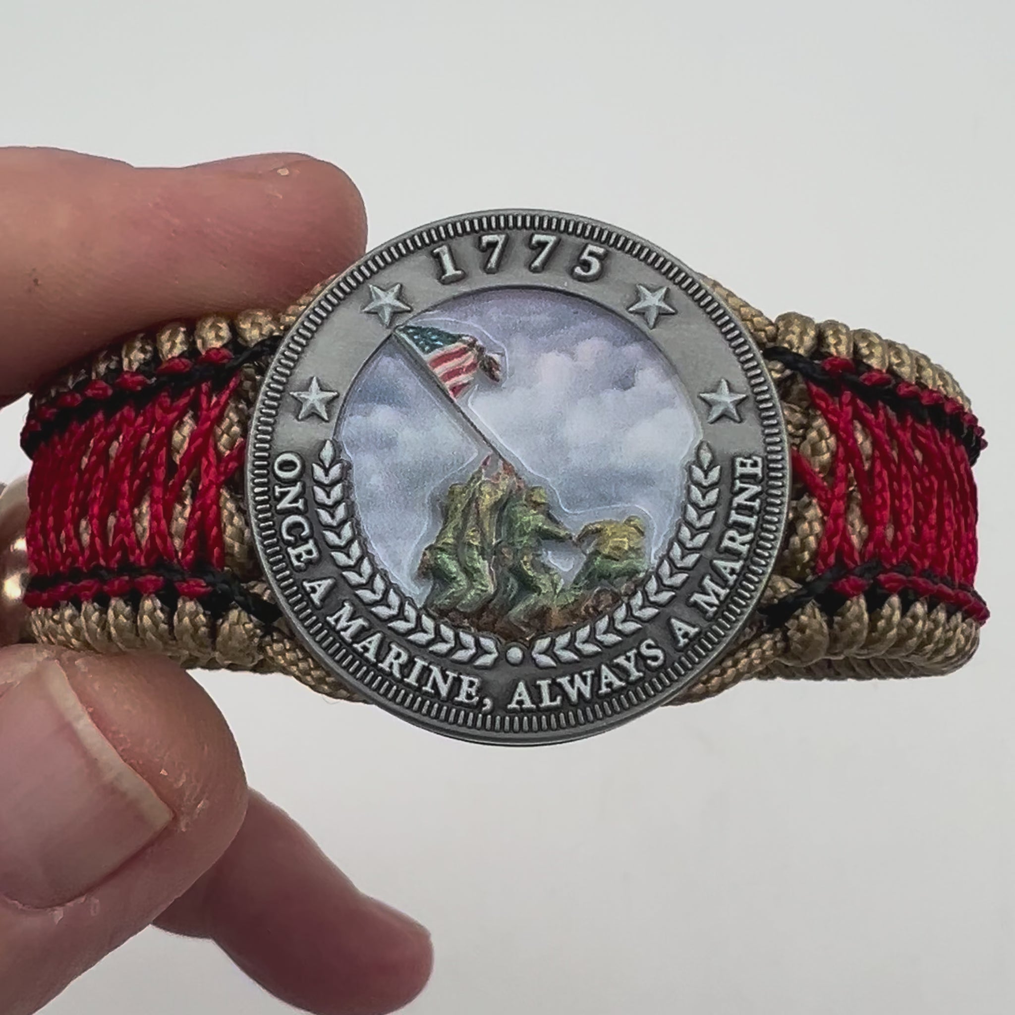 Thin, medium width, flexible and comfortable braided United States Marine Corps Iwo Jima bracelet featuring a UV painted antique silver plated Iwo Jima flag raising medallion, a gold Cobra style tactical buckle and woven with gold Type-1 paracord and Imperial Red and black nano cord.