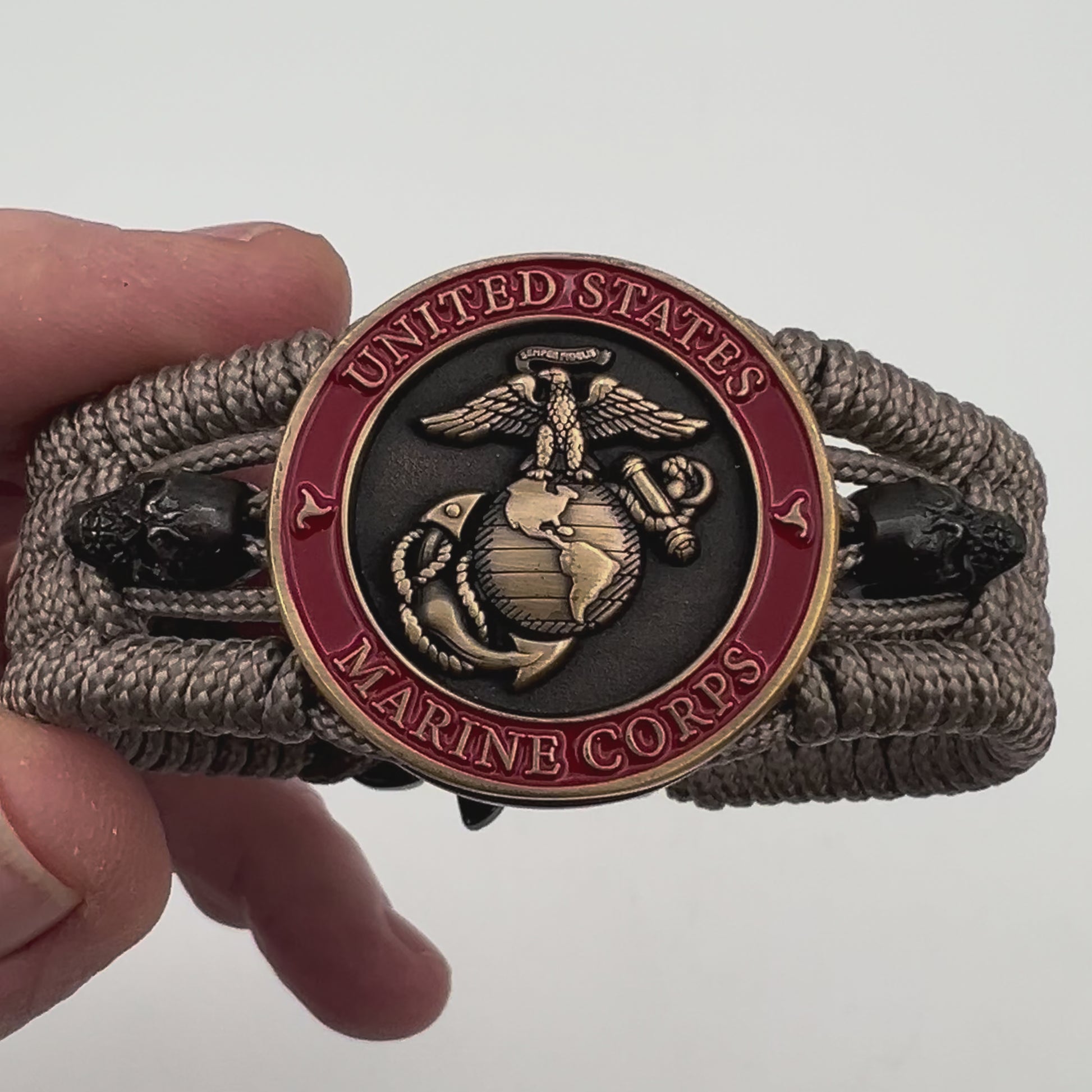 Thin, medium width, flexible and comfortable braided United States Marine Corps bracelet featuring a 24K antique gold plated USMC officer Eagle Globe and Anchor medallion, two black skulls, a black Cobra style tactical buckle and woven with tan Type-1 paracord.
