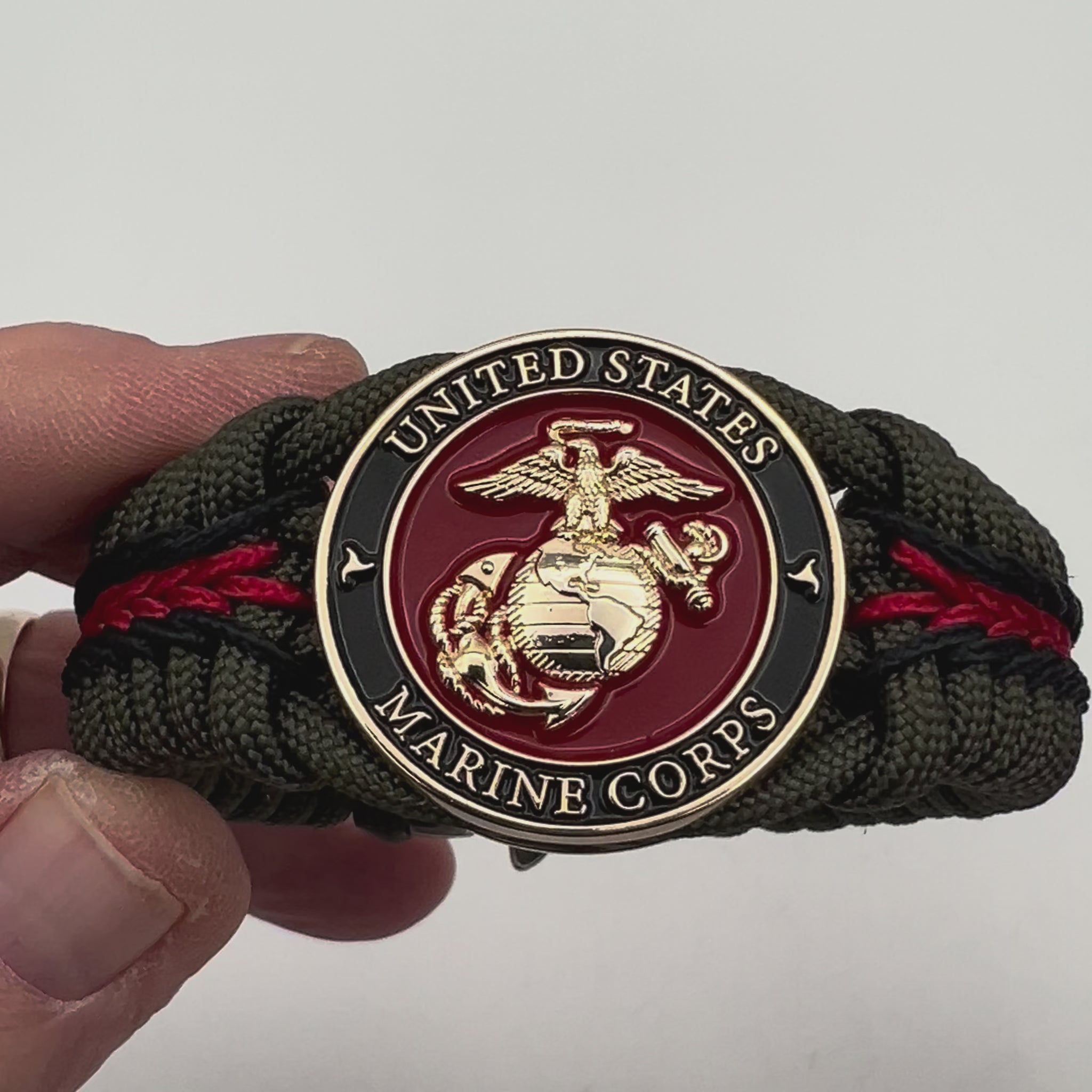 Thick, rigid and comfortable braided United States Marine Corps bracelet featuring a 24K gold plated USMC officer Eagle Globe and Anchor medallion, a gold Cobra style tactical buckle and woven with olive drab 550 paracord and black and Imperial red micro cord.