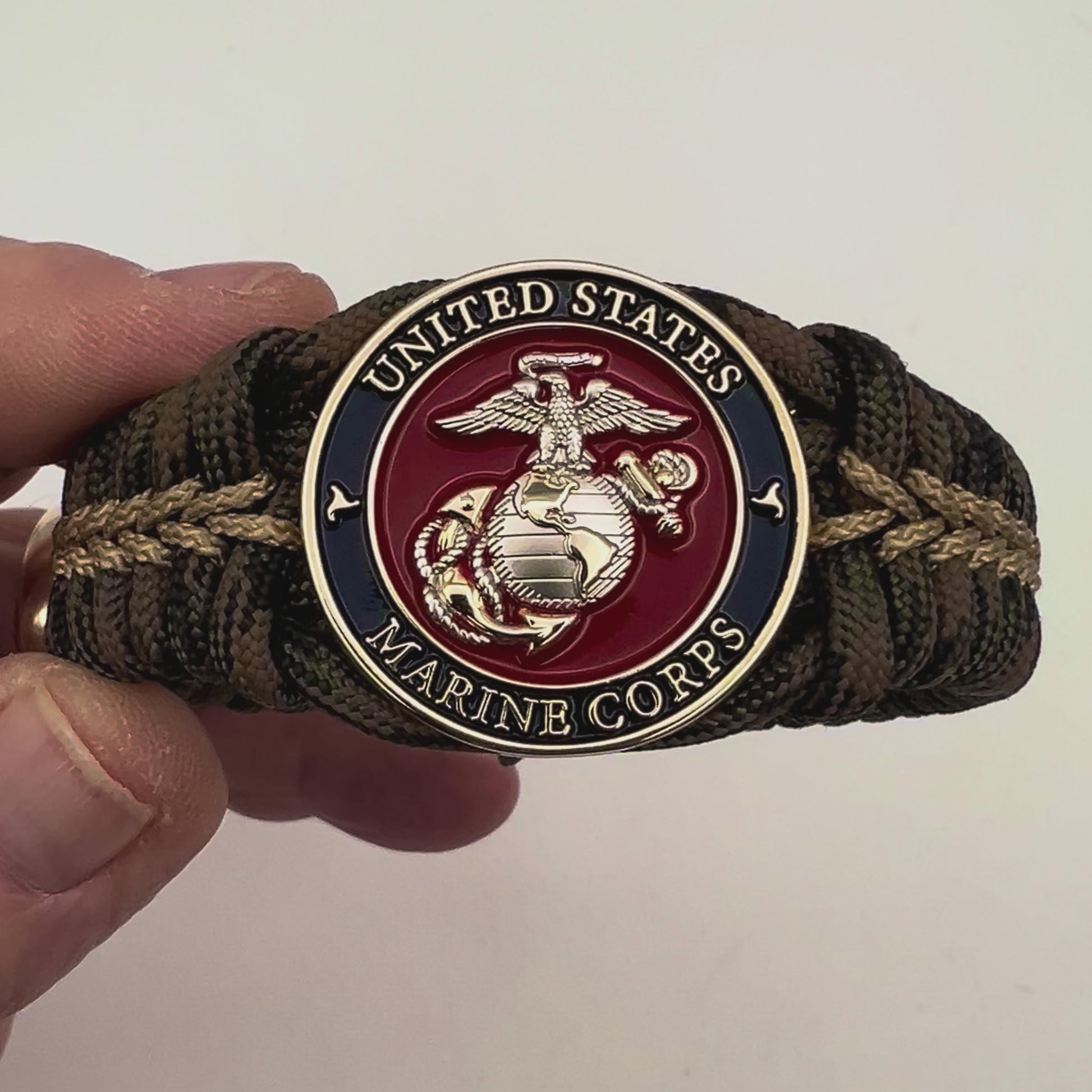 Thick, semi-rigid and comfortable braided United States Marine Corps bracelet featuring a 24K gold and silver plated USMC officer Eagle Globe and Anchor medallion, a gold Cobra style tactical buckle and woven with Woodland Camo 550 paracord and gold micro cord.