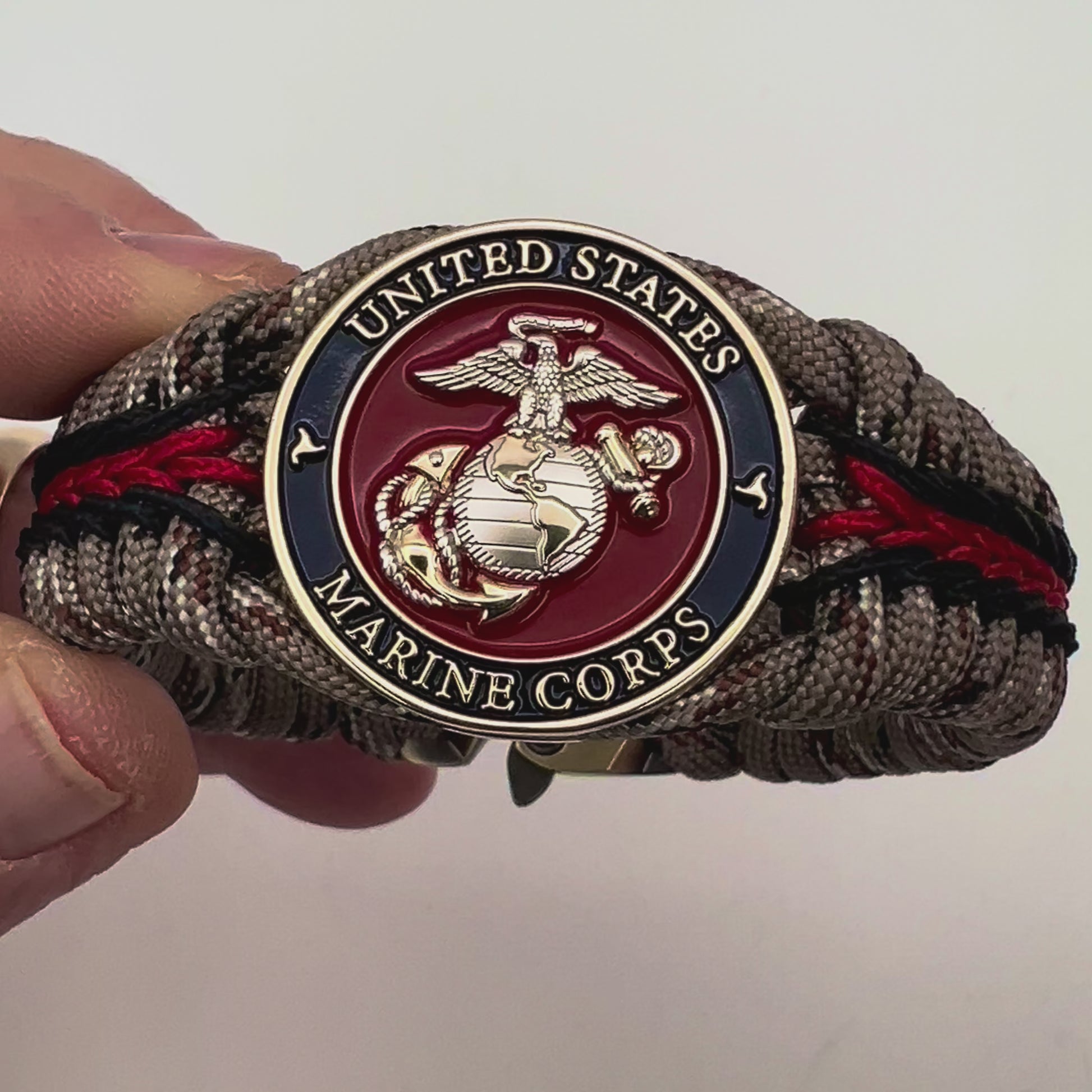 Thick and comfortable braided United States Marine Corps bracelet featuring a 24K gold and silver plated USMC officer Eagle Globe and Anchor medallion, a Cobra style tactical buckle and woven with Desert Camo 550 paracord and Imperial red and black micro cord.