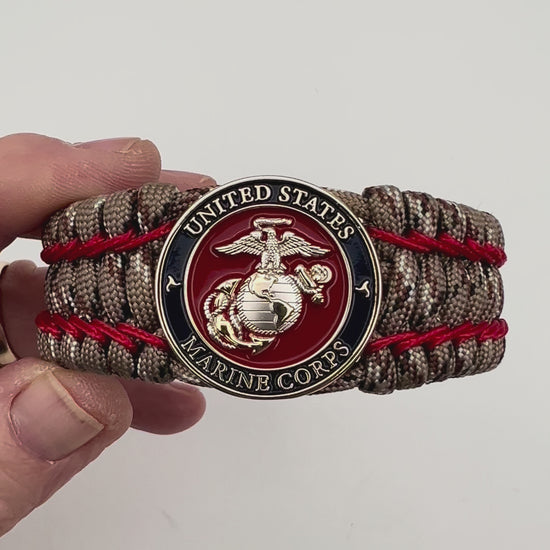 Thick and comfortable braided United States Marine Corps bracelet featuring a 24K gold and silver plated USMC officer Eagle Globe and Anchor medallion, a gold Cobra style tactical buckle and woven with Desert Camo 550 paracord and Imperial Red micro cord.