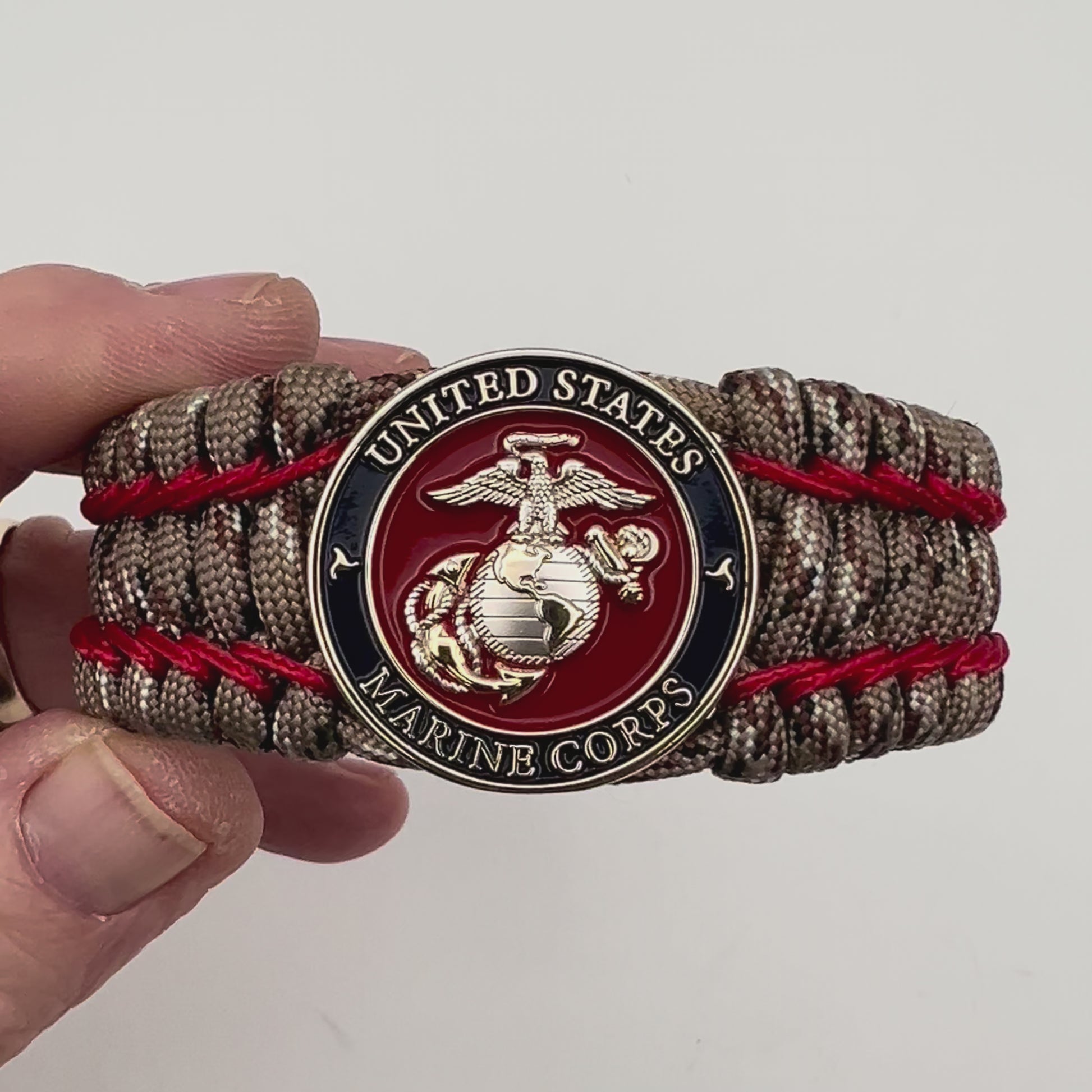 Thick and comfortable braided United States Marine Corps bracelet featuring a 24K gold and silver plated USMC officer Eagle Globe and Anchor medallion, a gold Cobra style tactical buckle and woven with Desert Camo 550 paracord and Imperial Red micro cord.