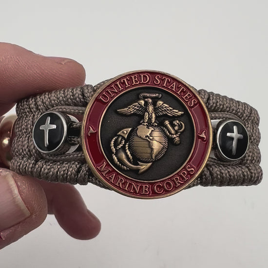 Thin, medium width, flexible and comfortable braided United States Marine Corps bracelet featuring a 24K antique gold plated USMC officer Eagle Globe and Anchor medallion, two Christian crosses, a black Cobra style tactical buckle and woven with Tan Type-1 paracord.