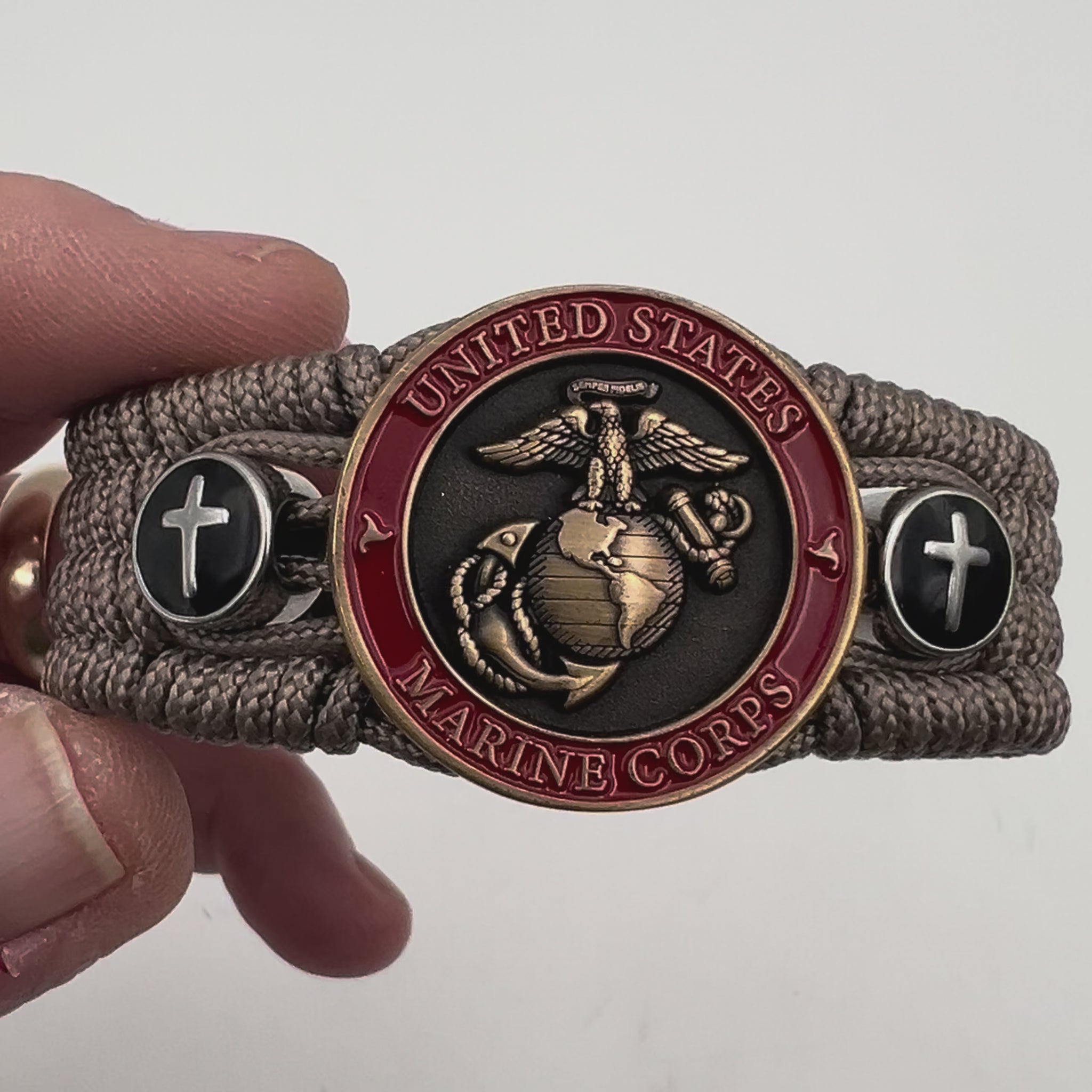 Thin, medium width, flexible and comfortable braided United States Marine Corps bracelet featuring a 24K antique gold plated USMC officer Eagle Globe and Anchor medallion, two Christian crosses, a black Cobra style tactical buckle and woven with Tan Type-1 paracord.