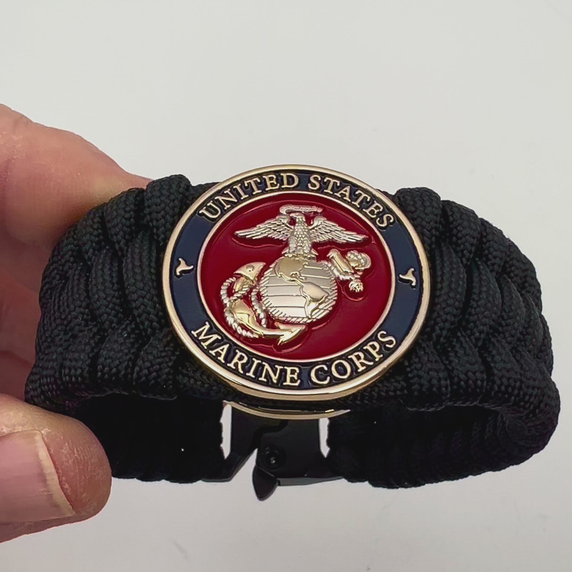 Thick and comfortable braided United States Marine Corps bracelet featuring a 24K gold and silver plated USMC officer Eagle Globe and Anchor medallion, a black Cobra style tactical buckle and woven with black 550 paracord.