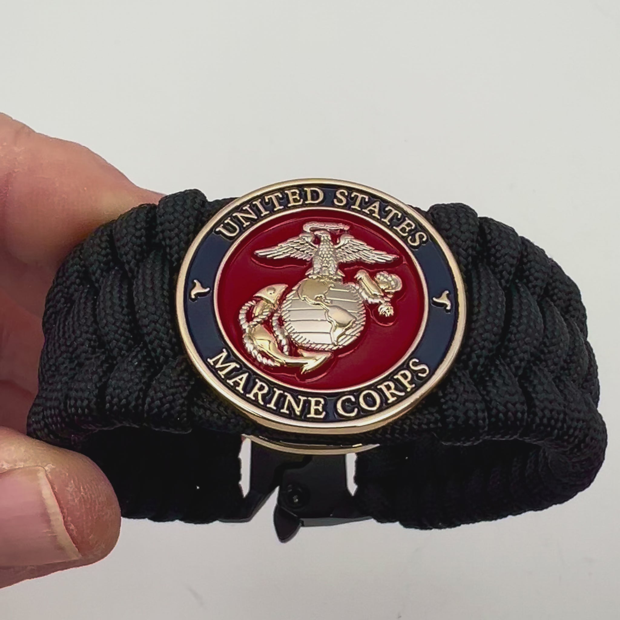 Thick and comfortable braided United States Marine Corps bracelet featuring a 24K gold and silver plated USMC officer Eagle Globe and Anchor medallion, a black Cobra style tactical buckle and woven with black 550 paracord.