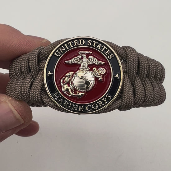 Thick, semi-rigid and comfortable braided United States Marine Corps bracelet featuring a 24K gold and silver plated USMC officer Eagle Globe and Anchor medallion, a gold Cobra style tactical buckle and woven with tan 550 paracord.