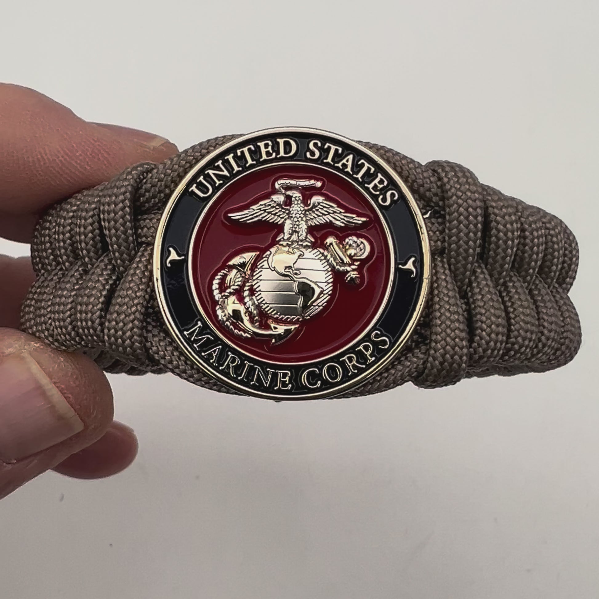 Thick, semi-rigid and comfortable braided United States Marine Corps bracelet featuring a 24K gold and silver plated USMC officer Eagle Globe and Anchor medallion, a gold Cobra style tactical buckle and woven with tan 550 paracord.