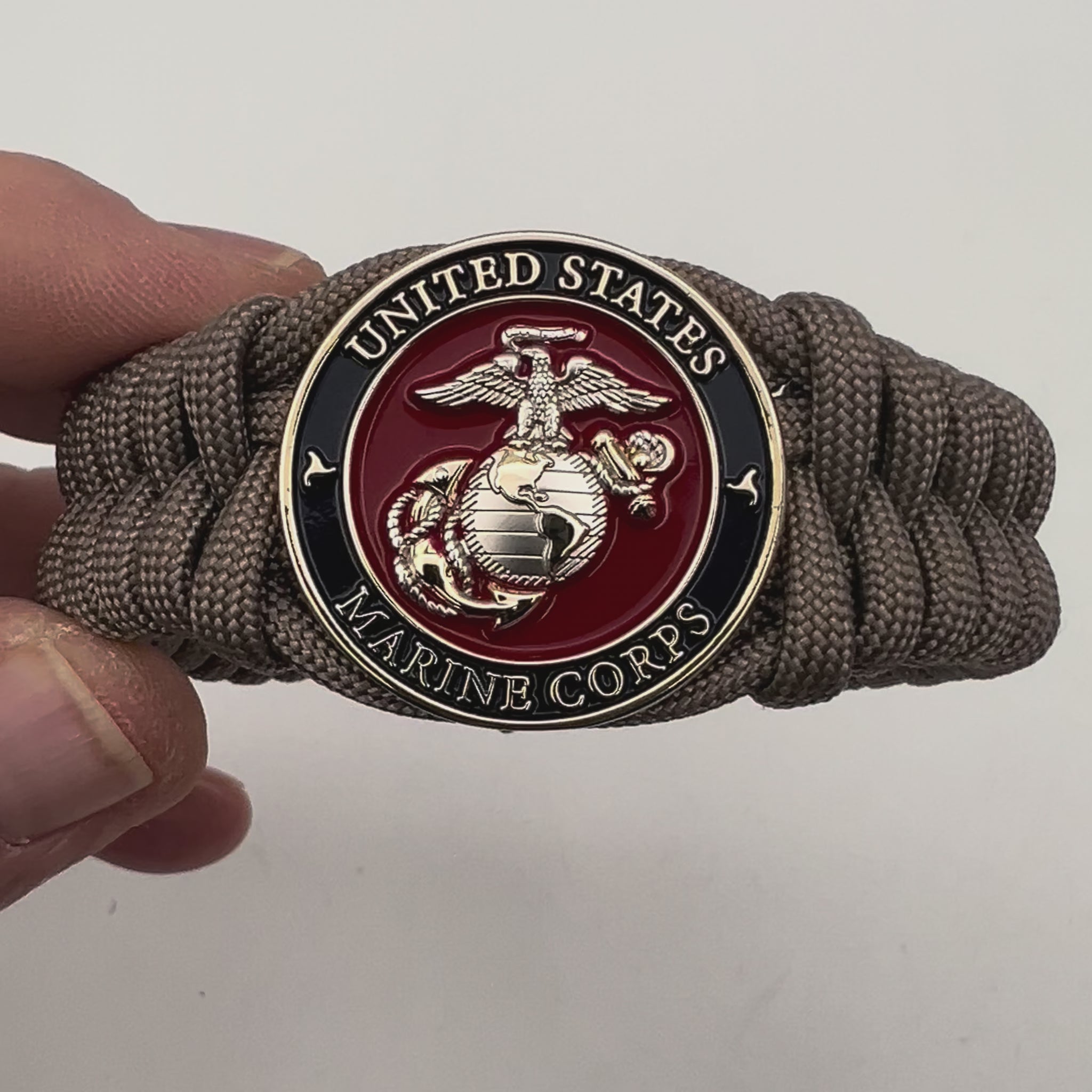 Thick, semi-rigid and comfortable braided United States Marine Corps bracelet featuring a 24K gold and silver plated USMC officer Eagle Globe and Anchor medallion, a gold Cobra style tactical buckle and woven with tan 550 paracord.