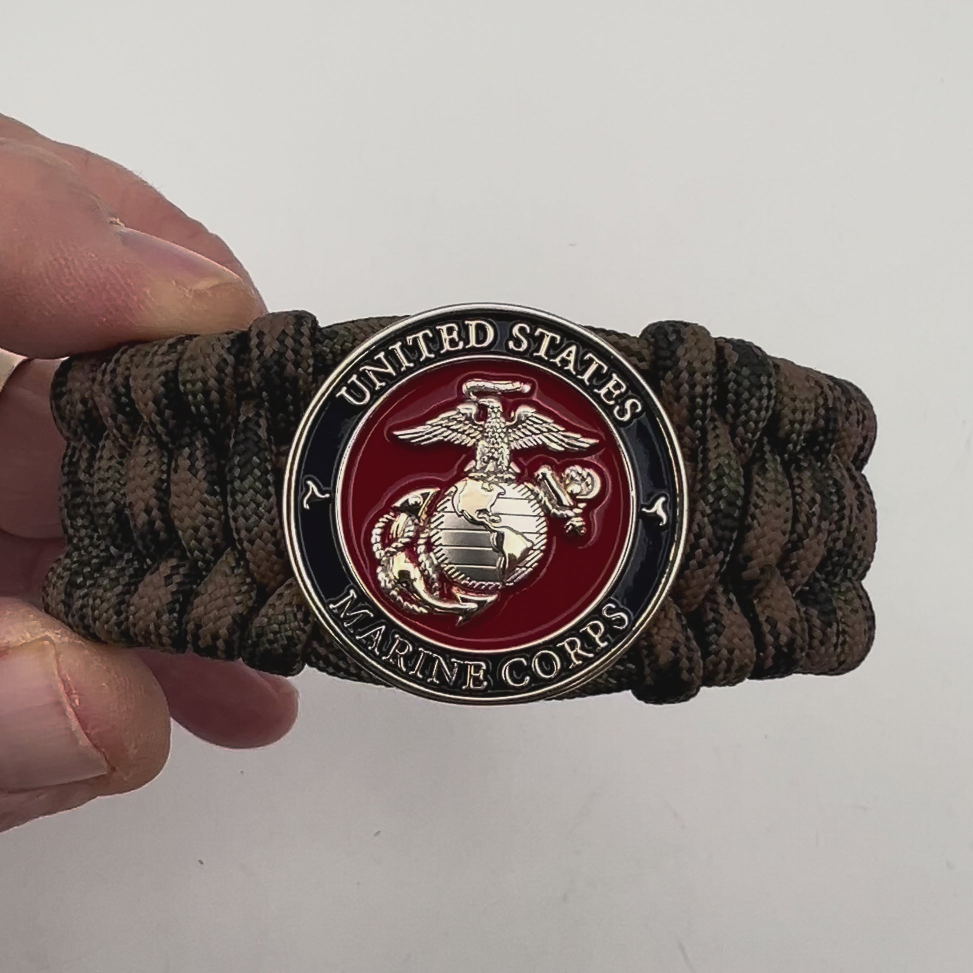 Thick, rigid and comfortable braided United States Marine Corps bracelet featuring a 24K gold and silver plated USMC officer Eagle Globe and Anchor medallion, a gold Cobra style tactical buckle and woven with Woodland Camo 550 paracord.