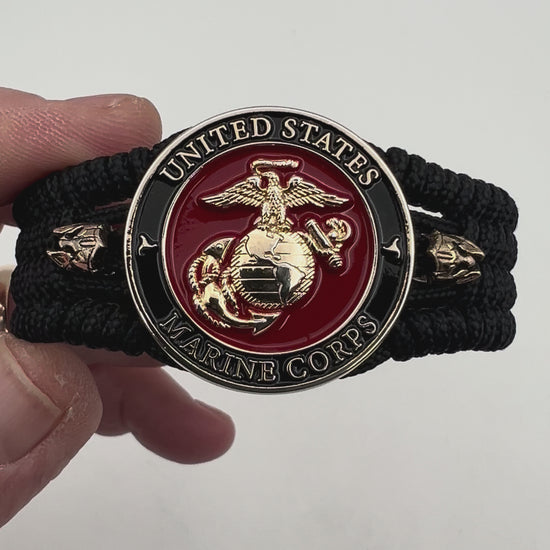 Thin, medium width, flexible and comfortable braided United States Marine Corps bracelet featuring a 24K gold plated USMC officer Eagle Globe and Anchor medallion, two brass Spartan helmets, a black Cobra style tactical buckle and woven with black Type-1 paracord.
