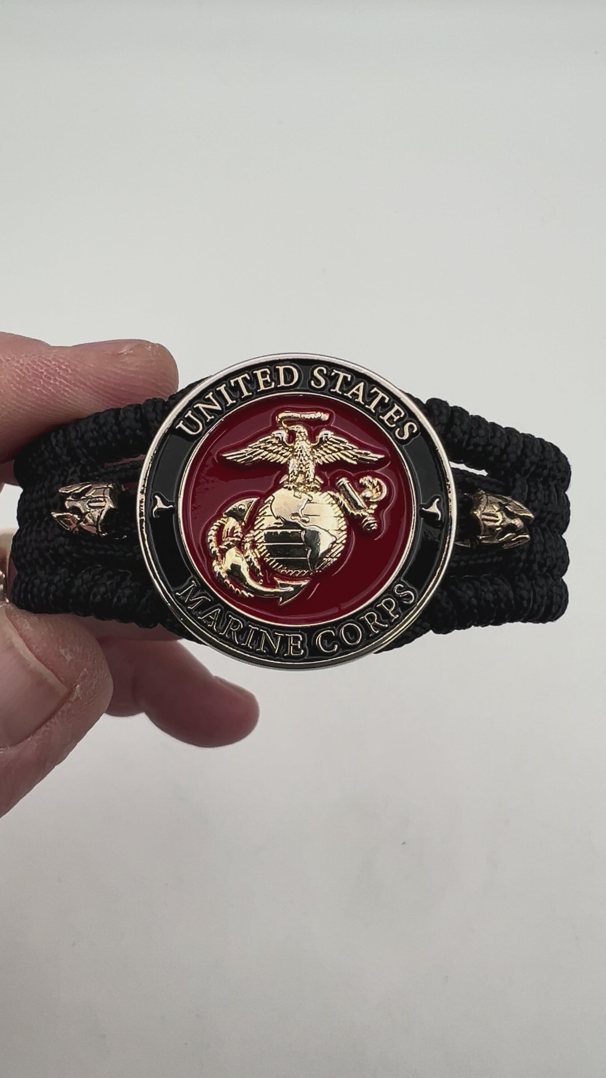 Thin, medium width, flexible and comfortable braided United States Marine Corps bracelet featuring a 24K gold plated USMC officer Eagle Globe and Anchor medallion, two brass Spartan helmets, a black Cobra style tactical buckle and woven with black Type-1 paracord.