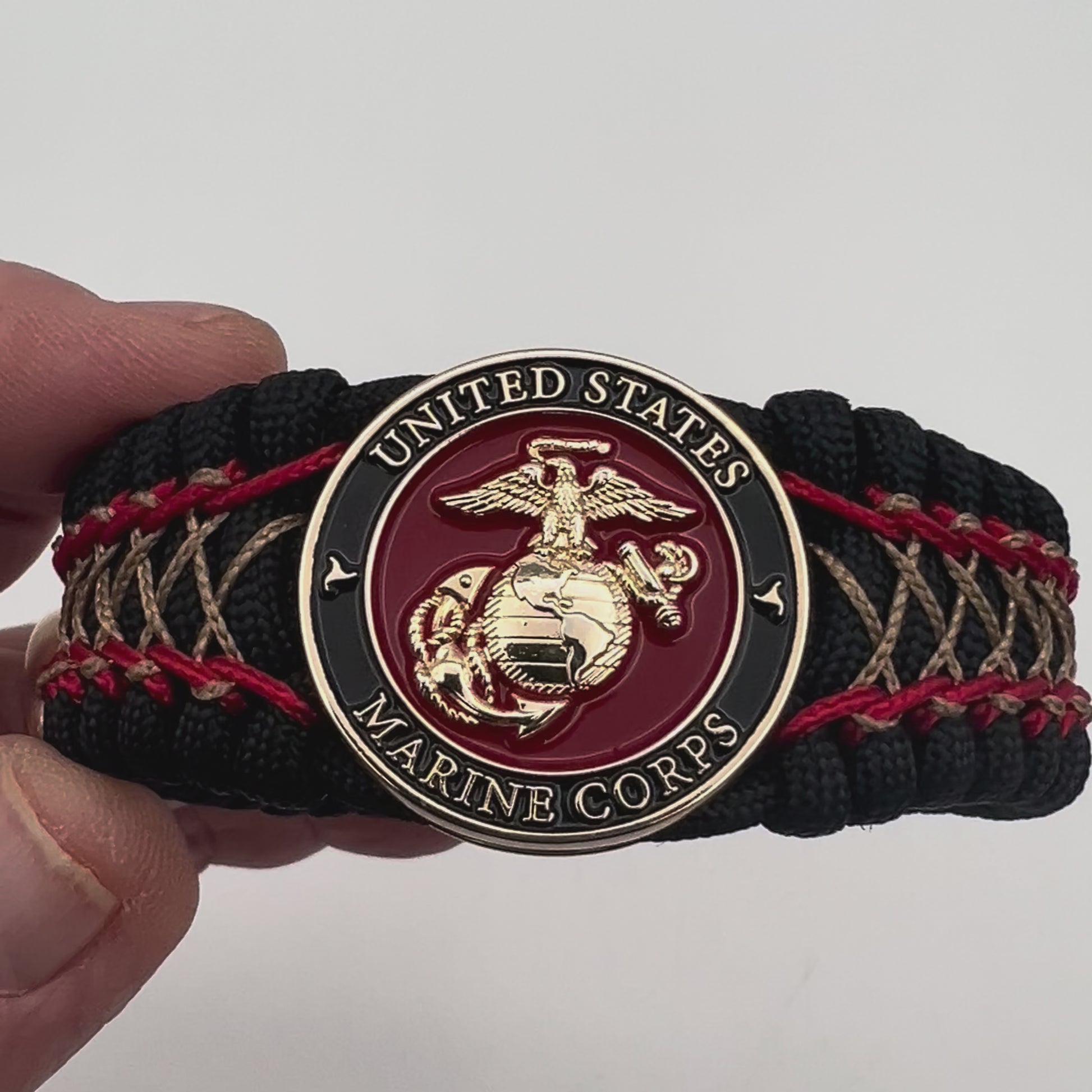 Thick, wide, rigid and comfortable braided United States Marine Corps bracelet featuring a 24K gold plated USMC Eagle Globe and Anchor medallion, a black Cobra style tactical buckle and woven with black 550 paracord and Imperial Red micro and gold nano cord.
