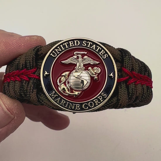 Thick, semi-rigid and comfortable braided United States Marine Corps bracelet featuring a 24K gold and silver plated USMC officer Eagle Globe and Anchor medallion, a gold Cobra style tactical buckle and woven with Woodland Camo 550 paracord and Imperial Red micro cord.