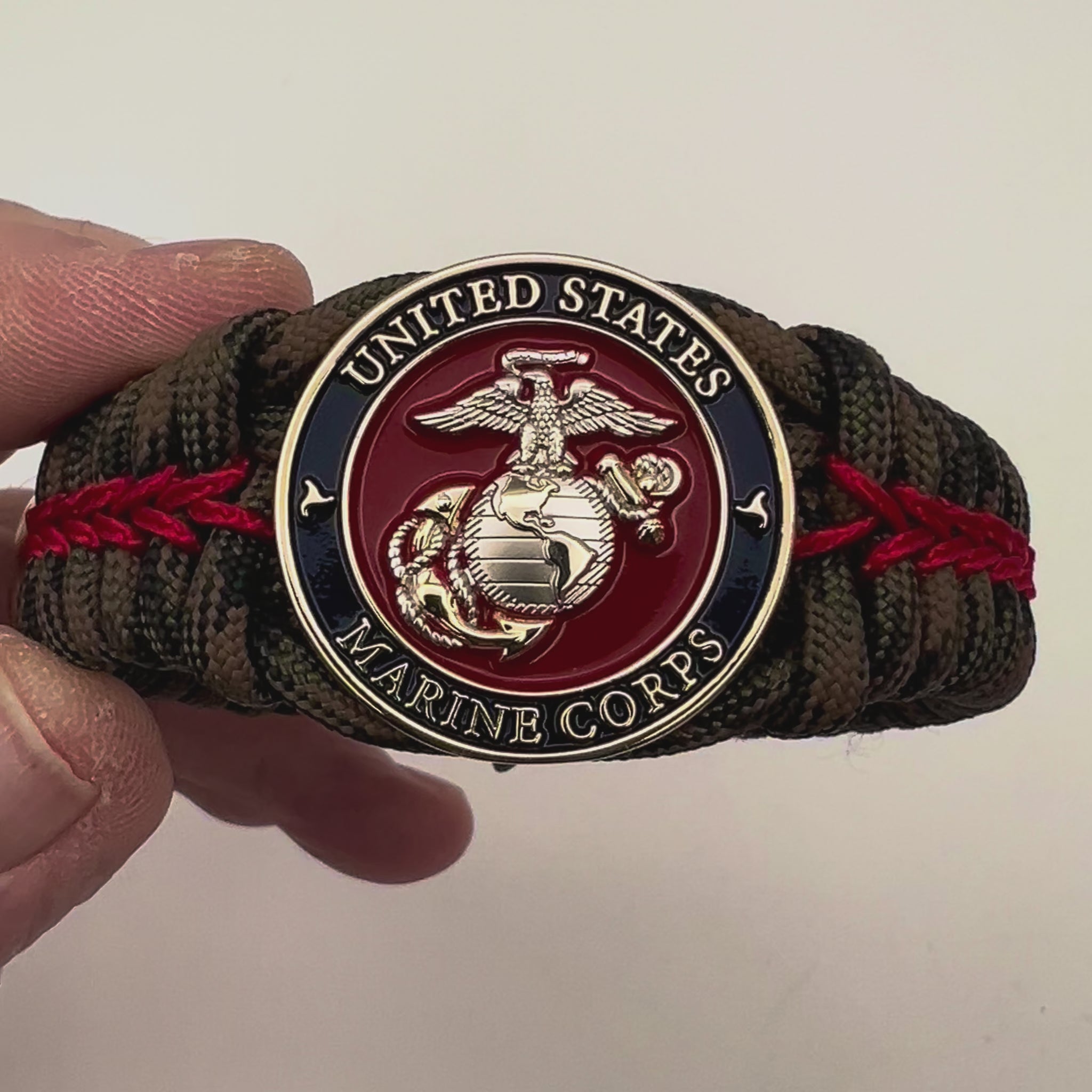 Thick, semi-rigid and comfortable braided United States Marine Corps bracelet featuring a 24K gold and silver plated USMC officer Eagle Globe and Anchor medallion, a gold Cobra style tactical buckle and woven with Woodland Camo 550 paracord and Imperial Red micro cord.