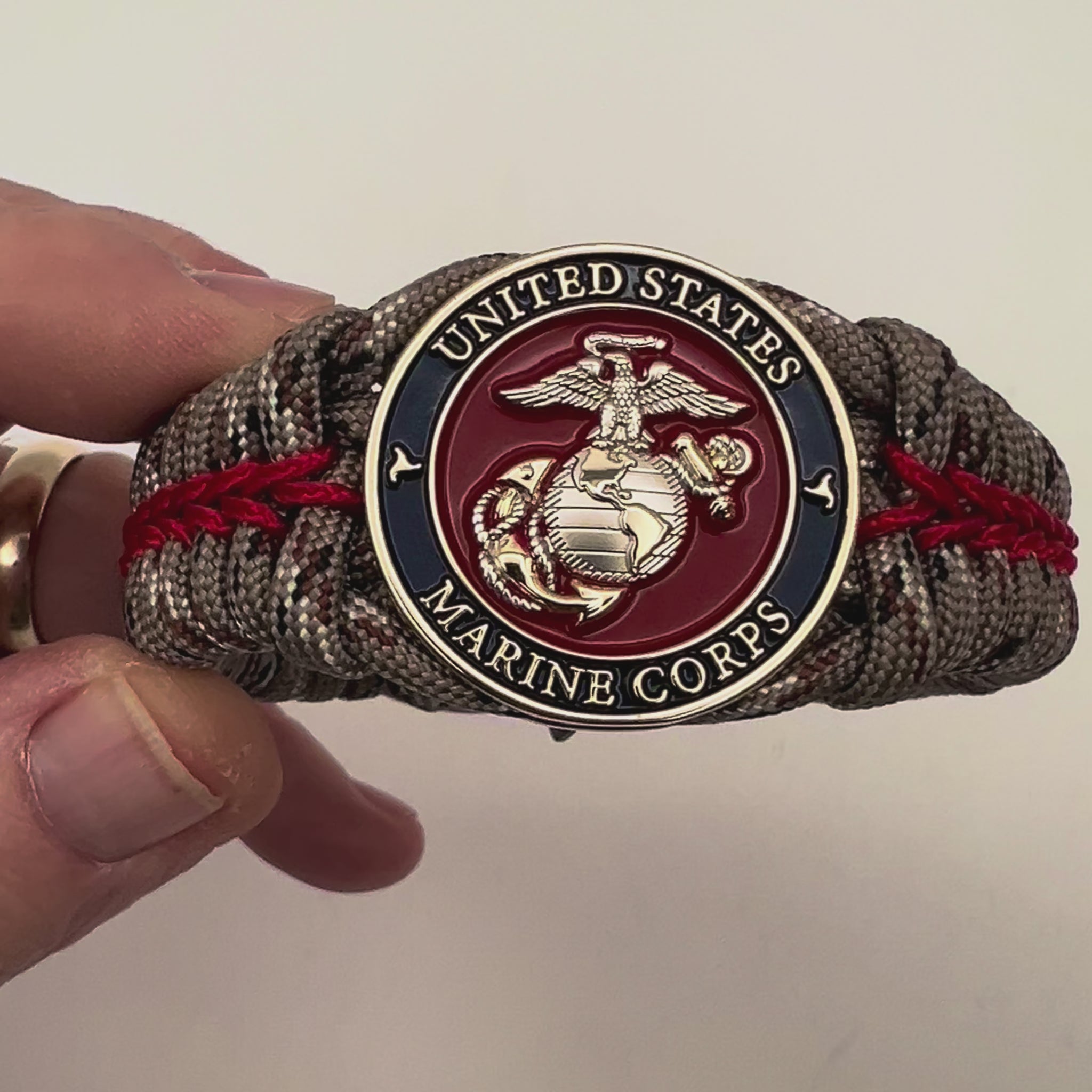 Thick and comfortable braided United States Marine Corps bracelet featuring a 24K gold and silver plated USMC officer Eagle Globe and Anchor medallion, a Cobra style tactical buckle and woven with Desert Camo 550 paracord and Imperial red micro cord.