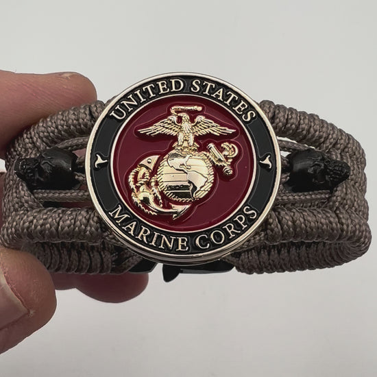 Thin, medium width, flexible and comfortable braided United States Marine Corps bracelet featuring a 24K gold plated USMC officer Eagle Globe and Anchor medallion, two black skulls, a black Cobra style tactical buckle and woven with tan Type-1 paracord.