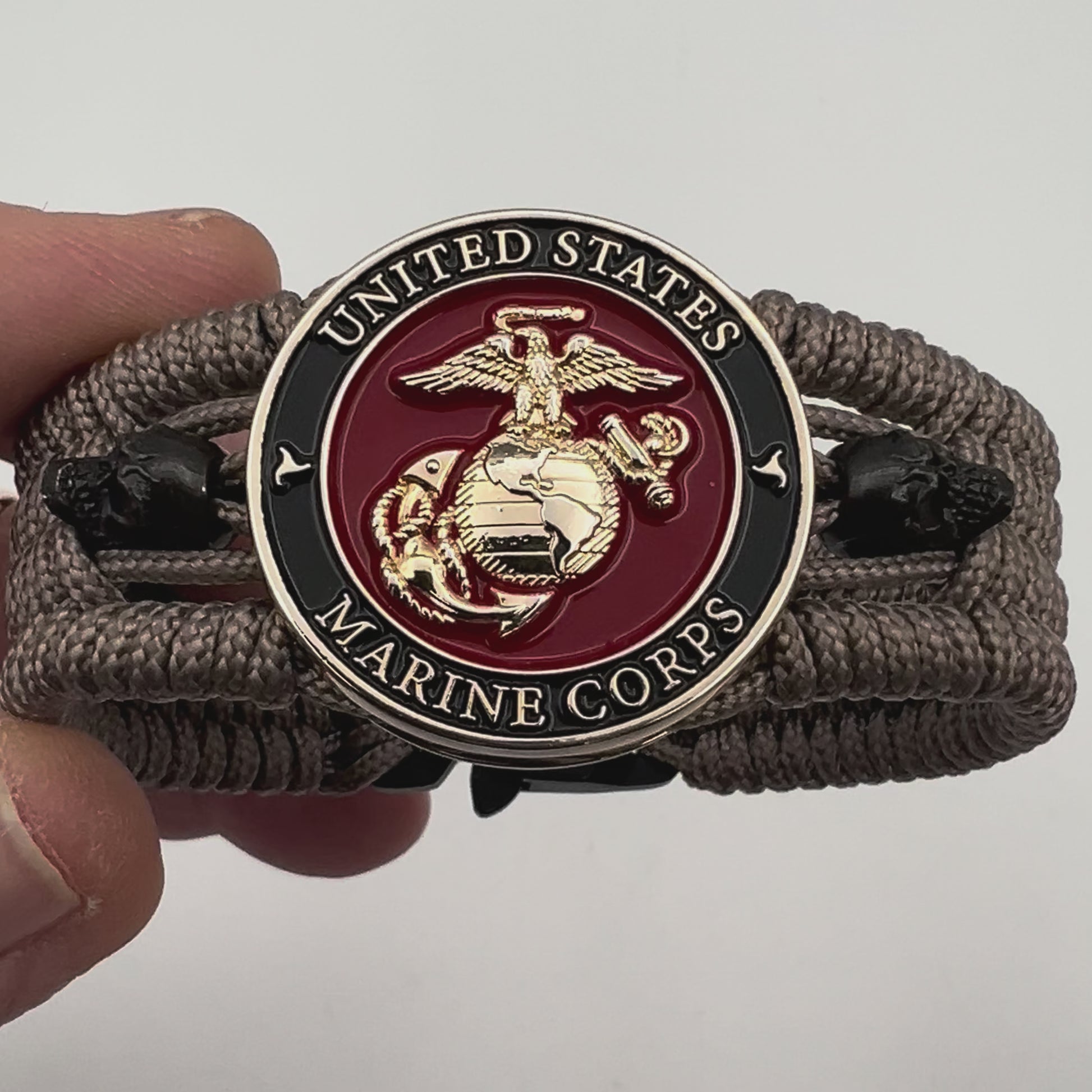 Thin, medium width, flexible and comfortable braided United States Marine Corps bracelet featuring a 24K gold plated USMC officer Eagle Globe and Anchor medallion, two black skulls, a black Cobra style tactical buckle and woven with tan Type-1 paracord.