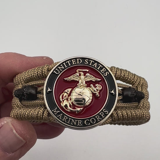 Thin, medium width, flexible and comfortable braided United States Marine Corps bracelet featuring a 24K gold plated USMC officer Eagle Globe and Anchor medallion, two black micro skulls, a gold Cobra style tactical buckle and woven with gold Type-1 paracord.