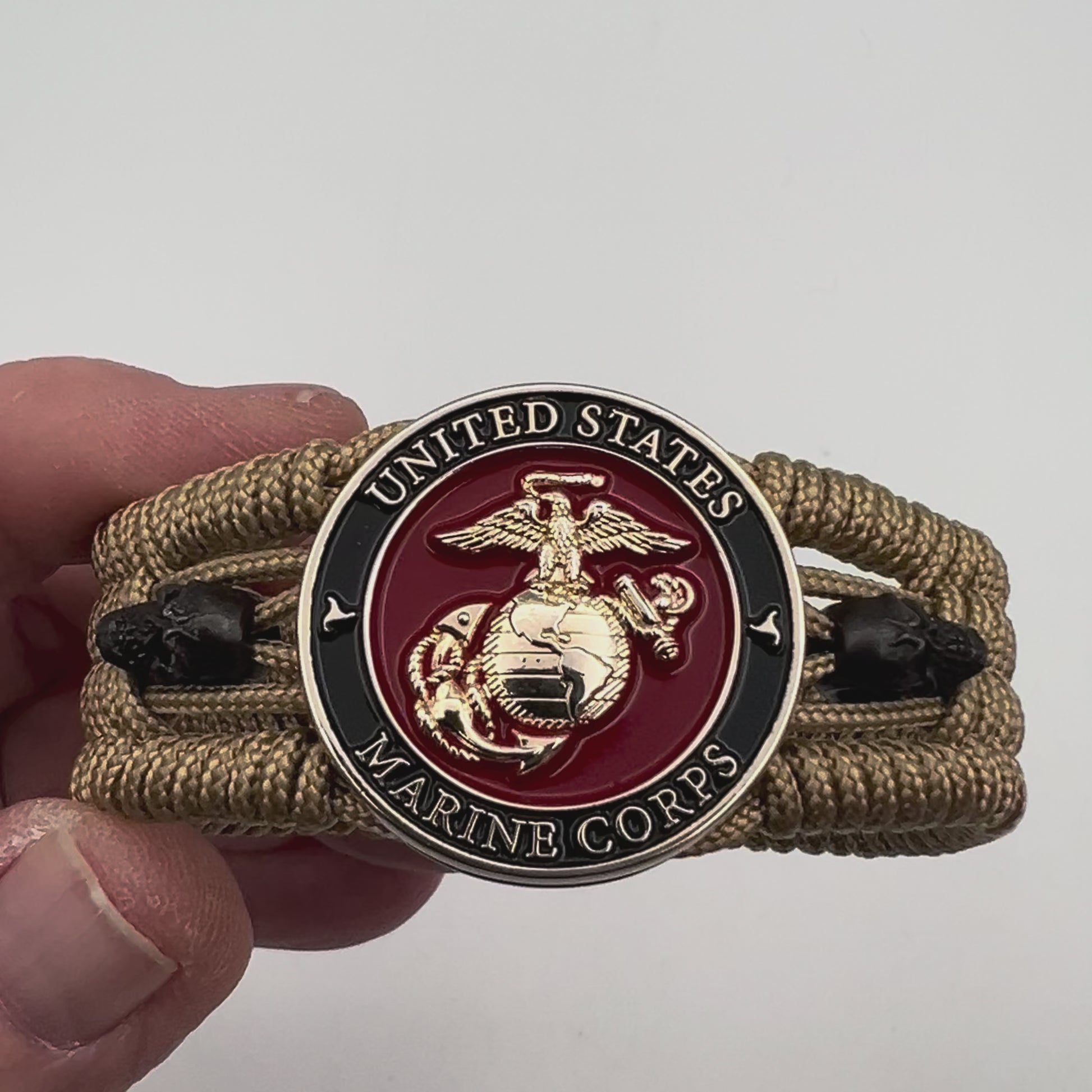 Thin, medium width, flexible and comfortable braided United States Marine Corps bracelet featuring a 24K gold plated USMC officer Eagle Globe and Anchor medallion, two black micro skulls, a gold Cobra style tactical buckle and woven with gold Type-1 paracord.