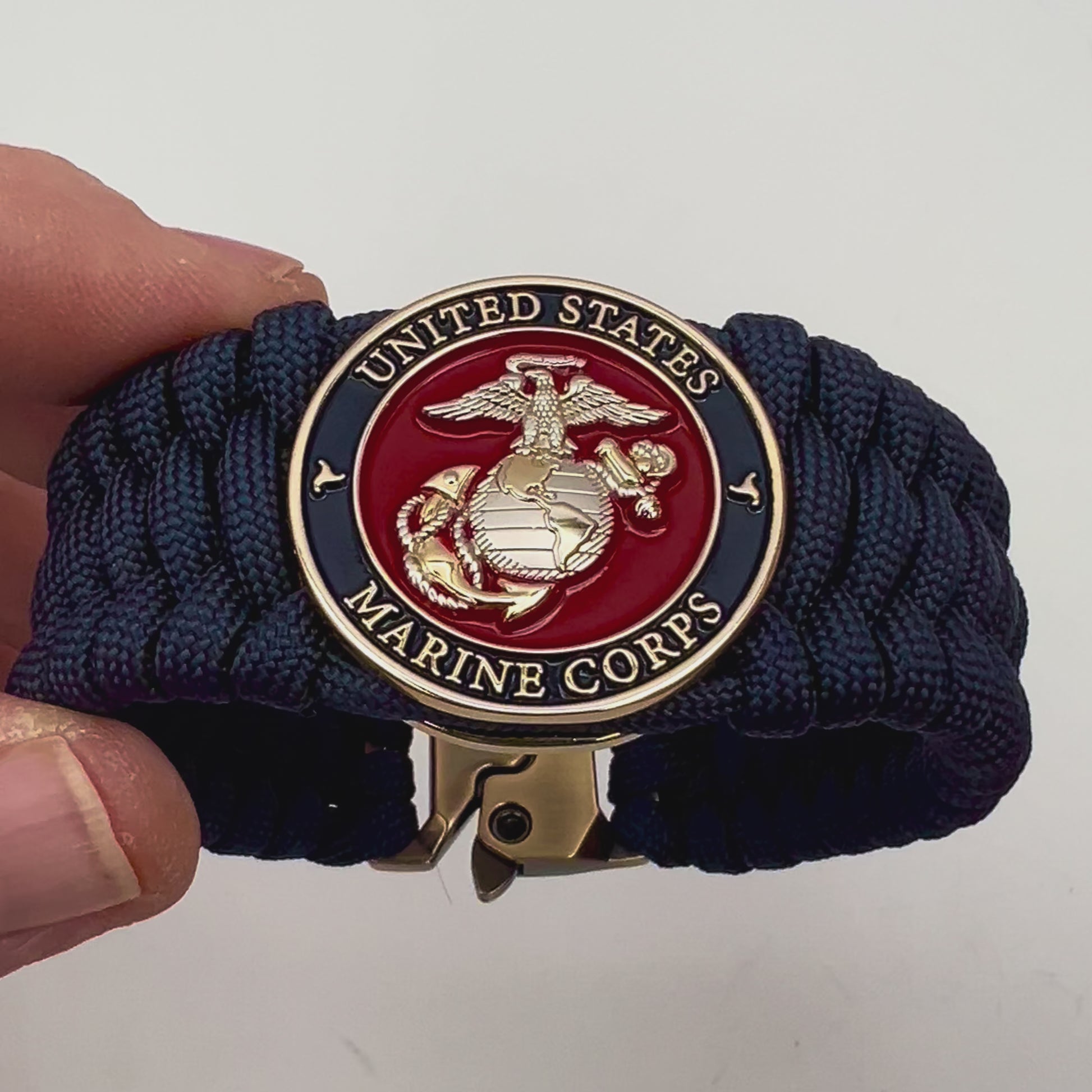 Thick and comfortable braided United States Marine Corps bracelet featuring a 24K gold and silver plated USMC officer Eagle Globe and Anchor medallion, a Cobra style tactical buckle and woven with Navy Blue 550 paracord.