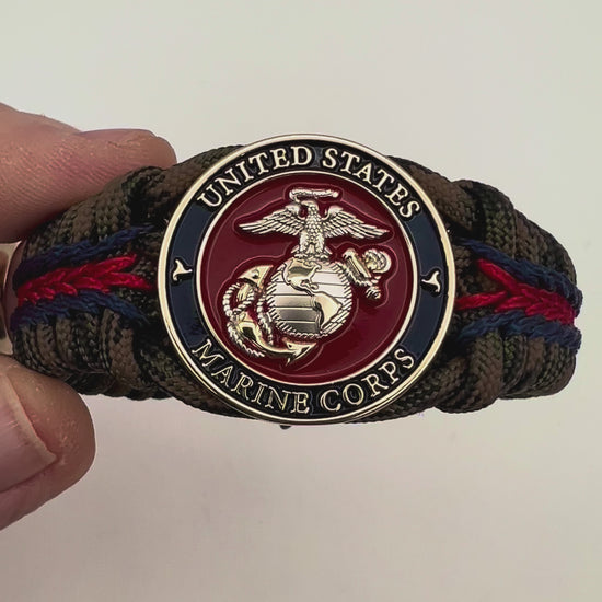 Thick, semi-rigid and comfortable braided United States Marine Corps bracelet featuring a 24K gold and silver plated USMC officer Eagle Globe and Anchor medallion, a gold Cobra style tactical buckle and woven with Woodland Camo 550 paracord and Imperial Red and Navy Blue micro cord.